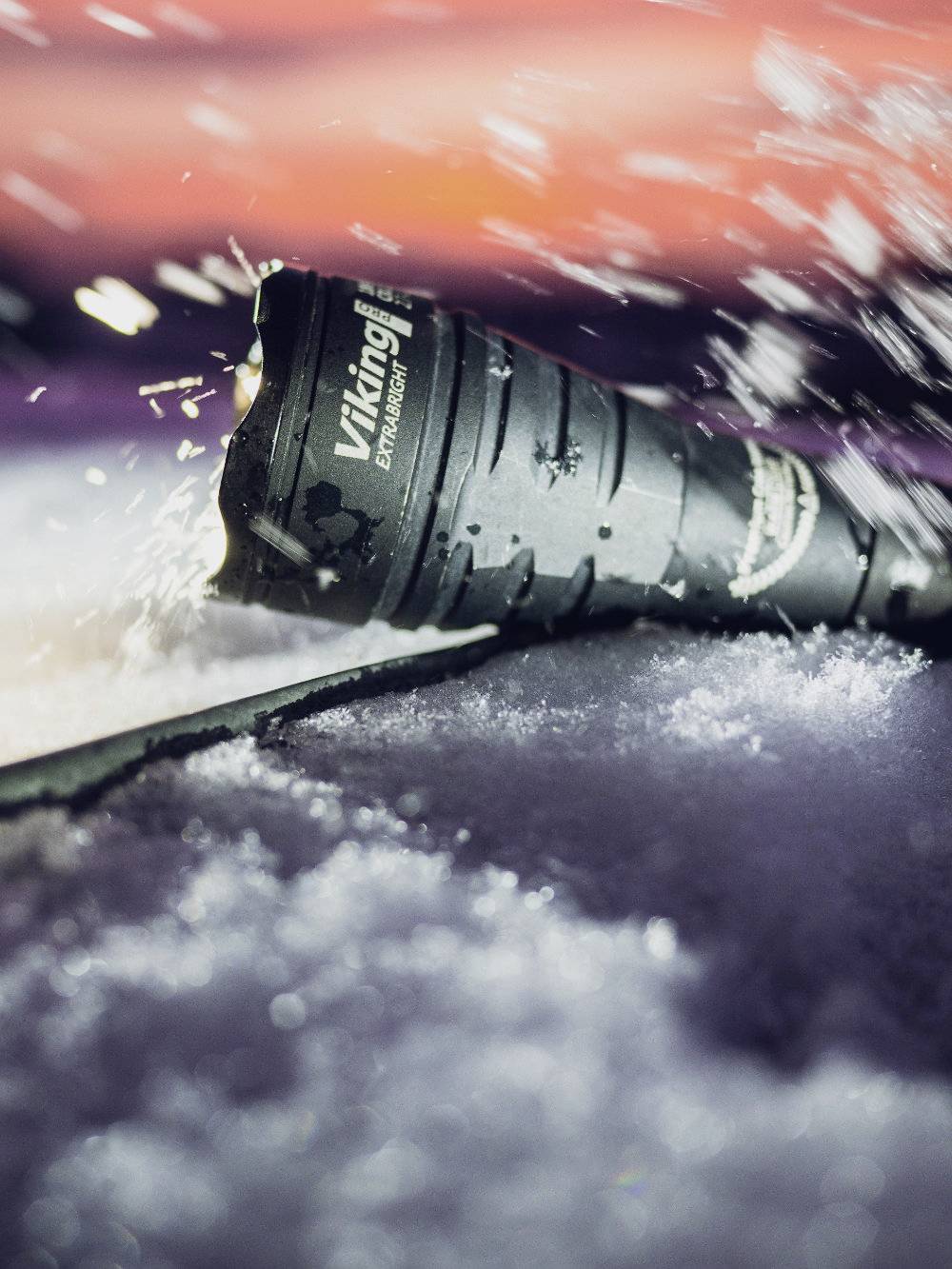 Torch lies in snow, surrounded by splashing water. The background is blurred and shows vivid red hues.