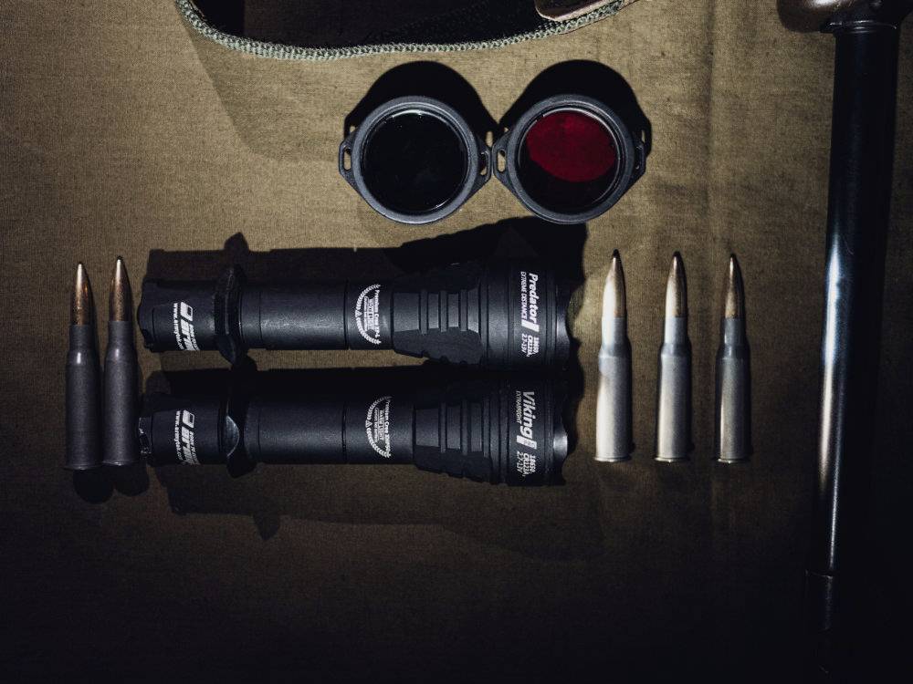 Two tactical torches and six cartridges (some unused) are lying on a brown cloth. Two lens covers are open.