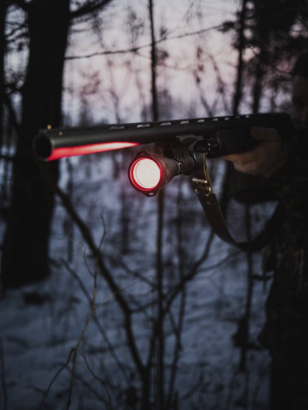A person in the woods with a long torch at dusk, the red beam of light shining towards the viewer.