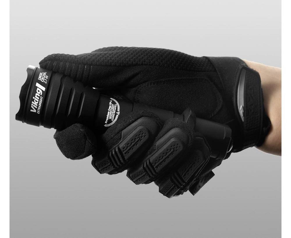 A hand in a black, padded glove is holding a small torch. The torch has a robust surface.