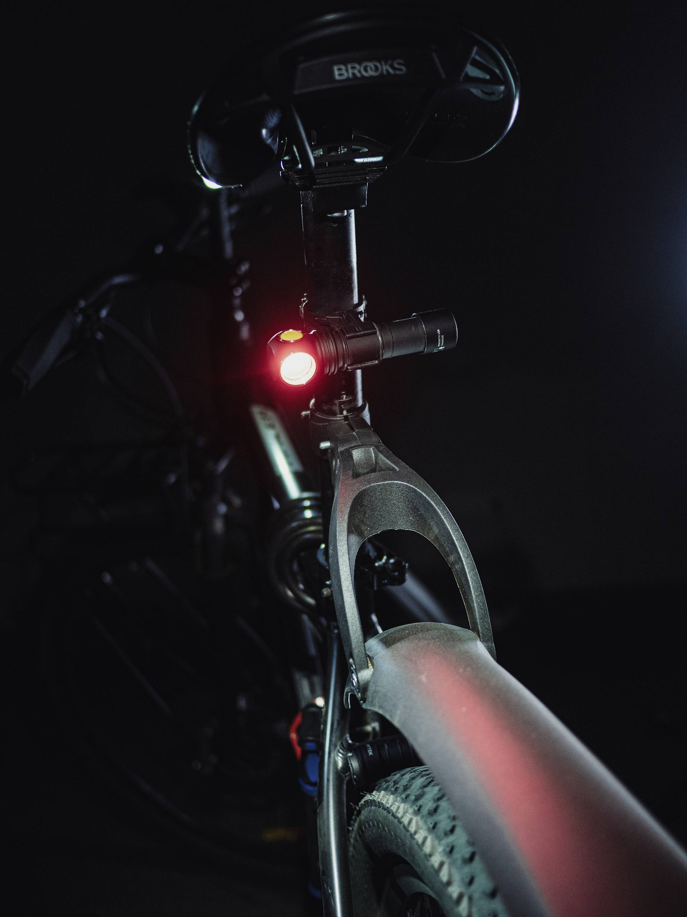 A bicycle in the darkness, illuminated by a red rear light beneath the saddle. The focus is on the safety aspect of the light.