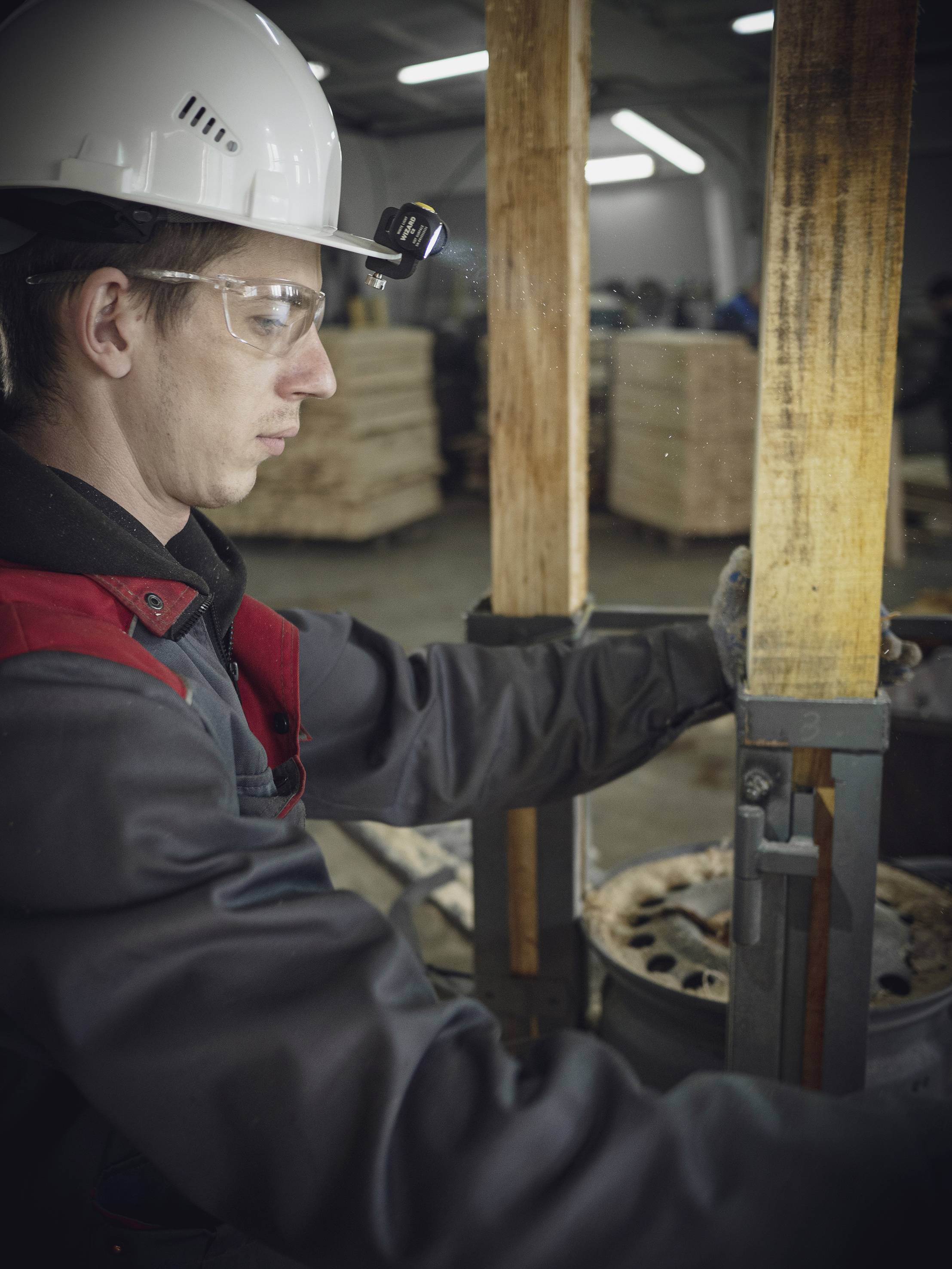 A worker in protective clothing is operating a machine in a factory hall. Wooden pallets can be seen in the background.