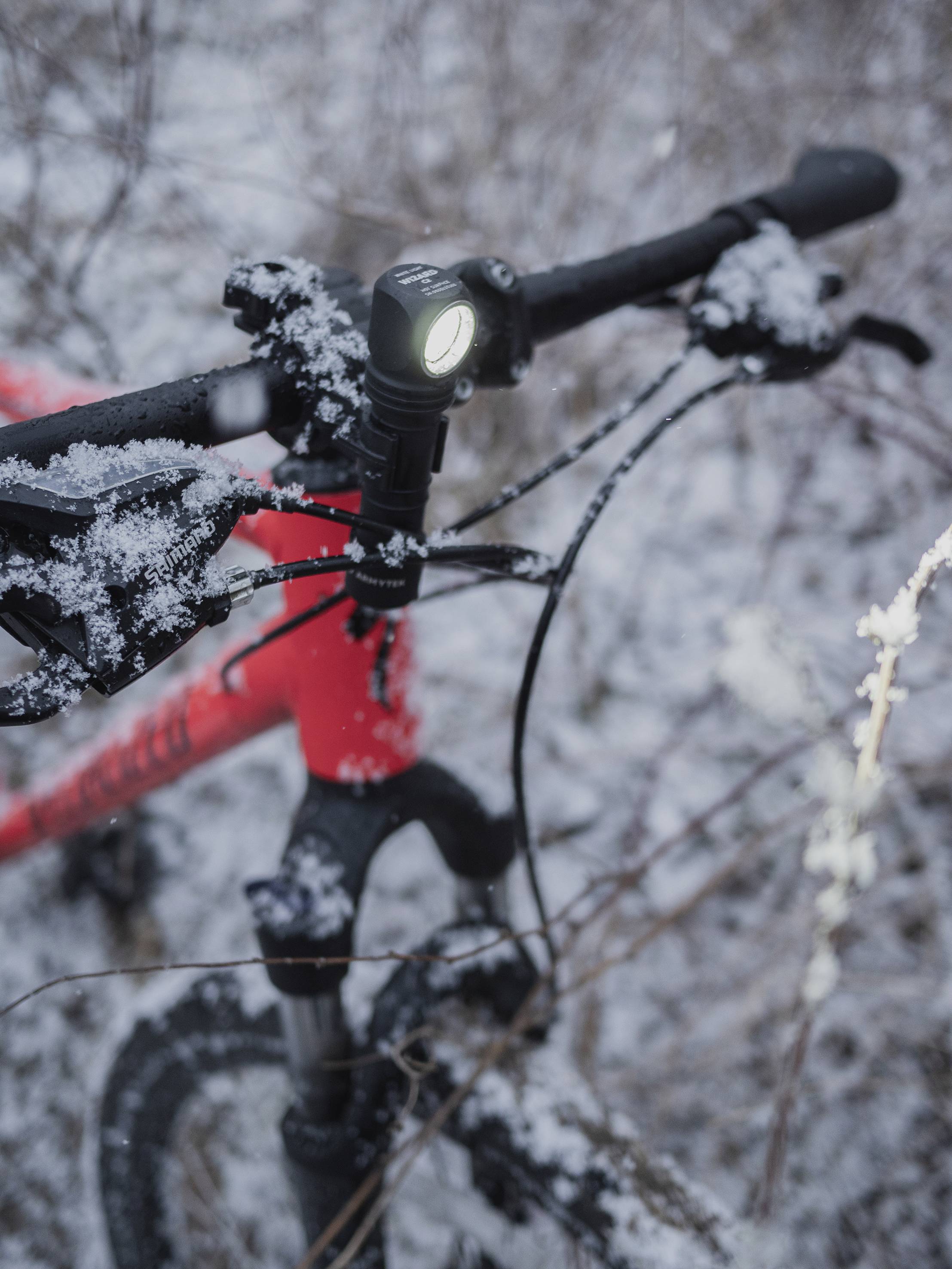 Red bicycle in the snow, front light switched on. Bicycle handlebars and frame are covered in snow. Wintry outdoor scene.