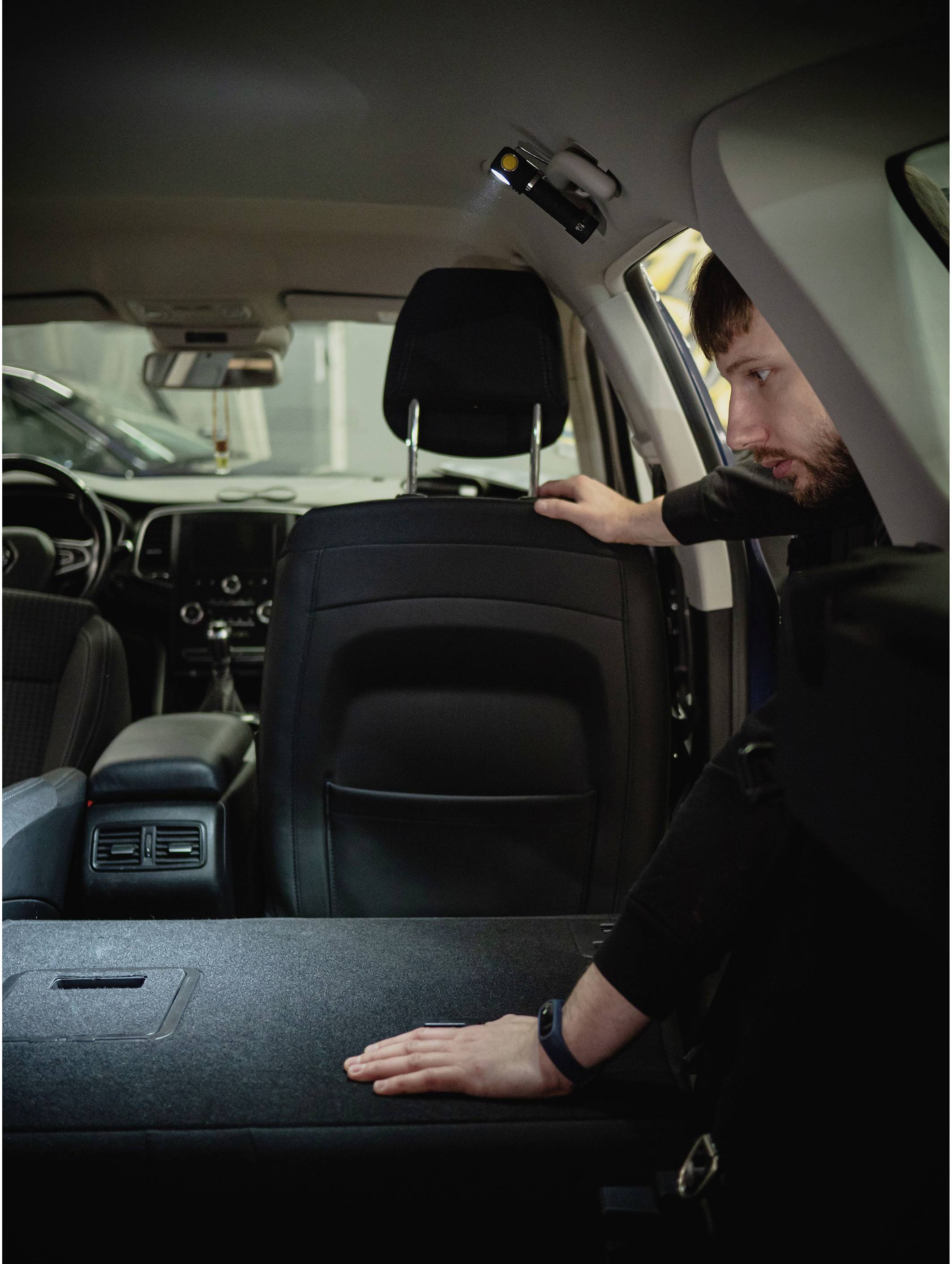 A man in a car is checking the folded-down rear seat to increase the boot space.