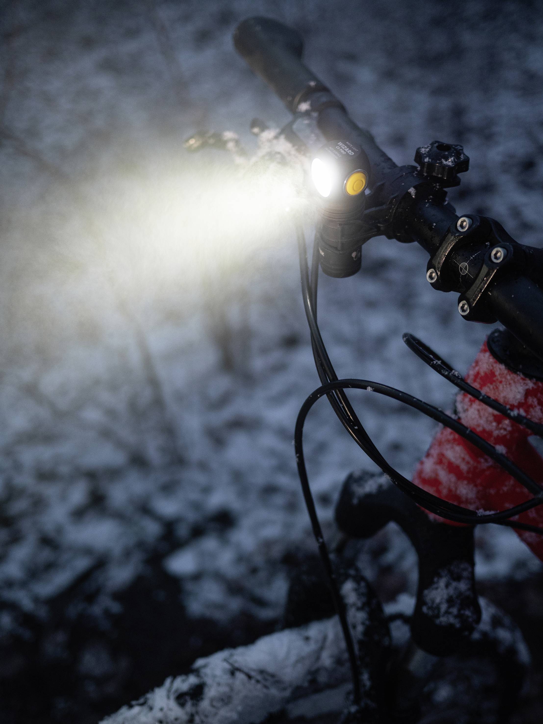 A cyclist in the snow with a front light switched on, brightly illuminating the path in the twilight.
