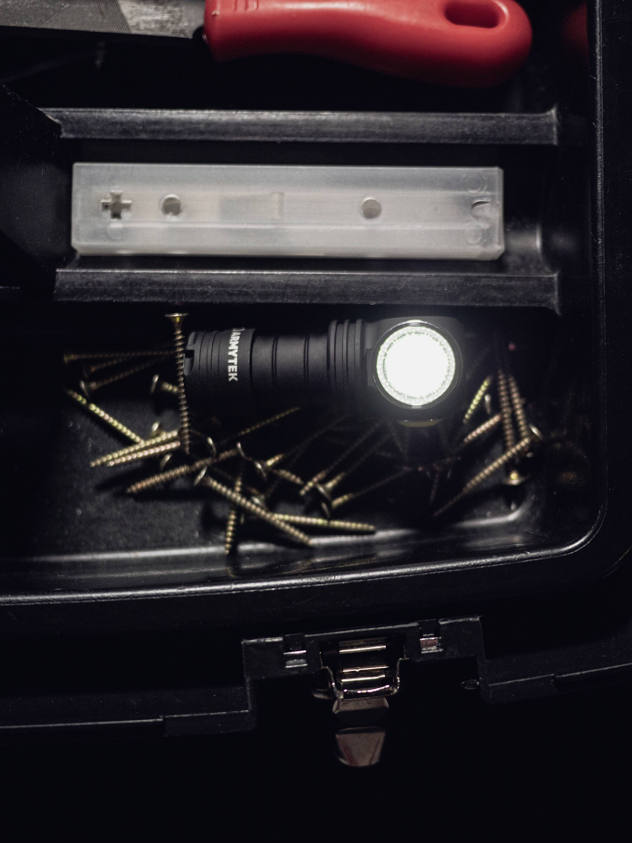 A toolbox with screws, a torch, and a red screwdriver handle. The torch is emitting bright light.