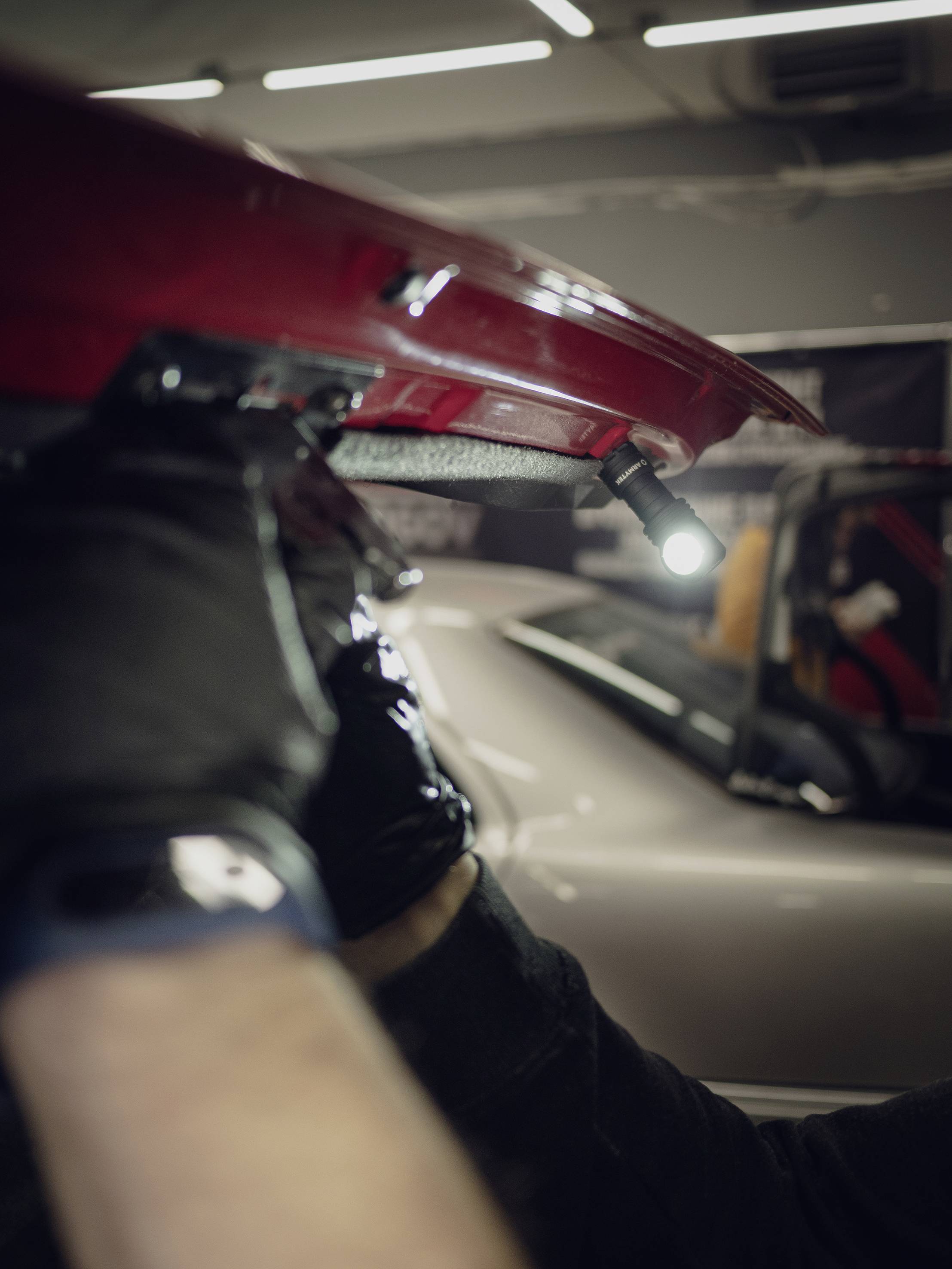 A person is wearing black gloves and repairing the interior of a red car roof, with a lamp illuminating the work area.