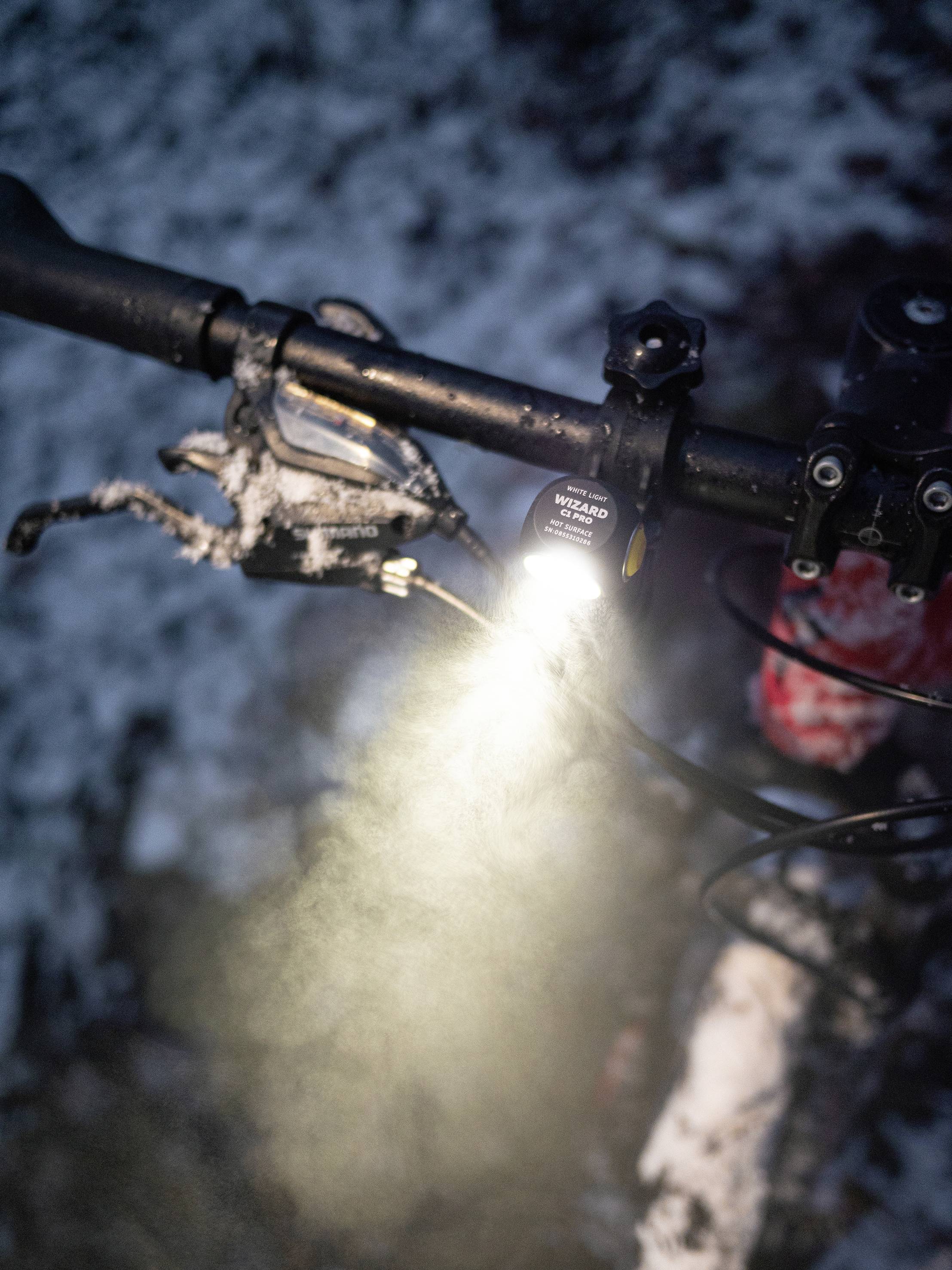 Bicycle handlebars with a light switched on in the darkness, surrounded by snow, indicates a journey in winter conditions.