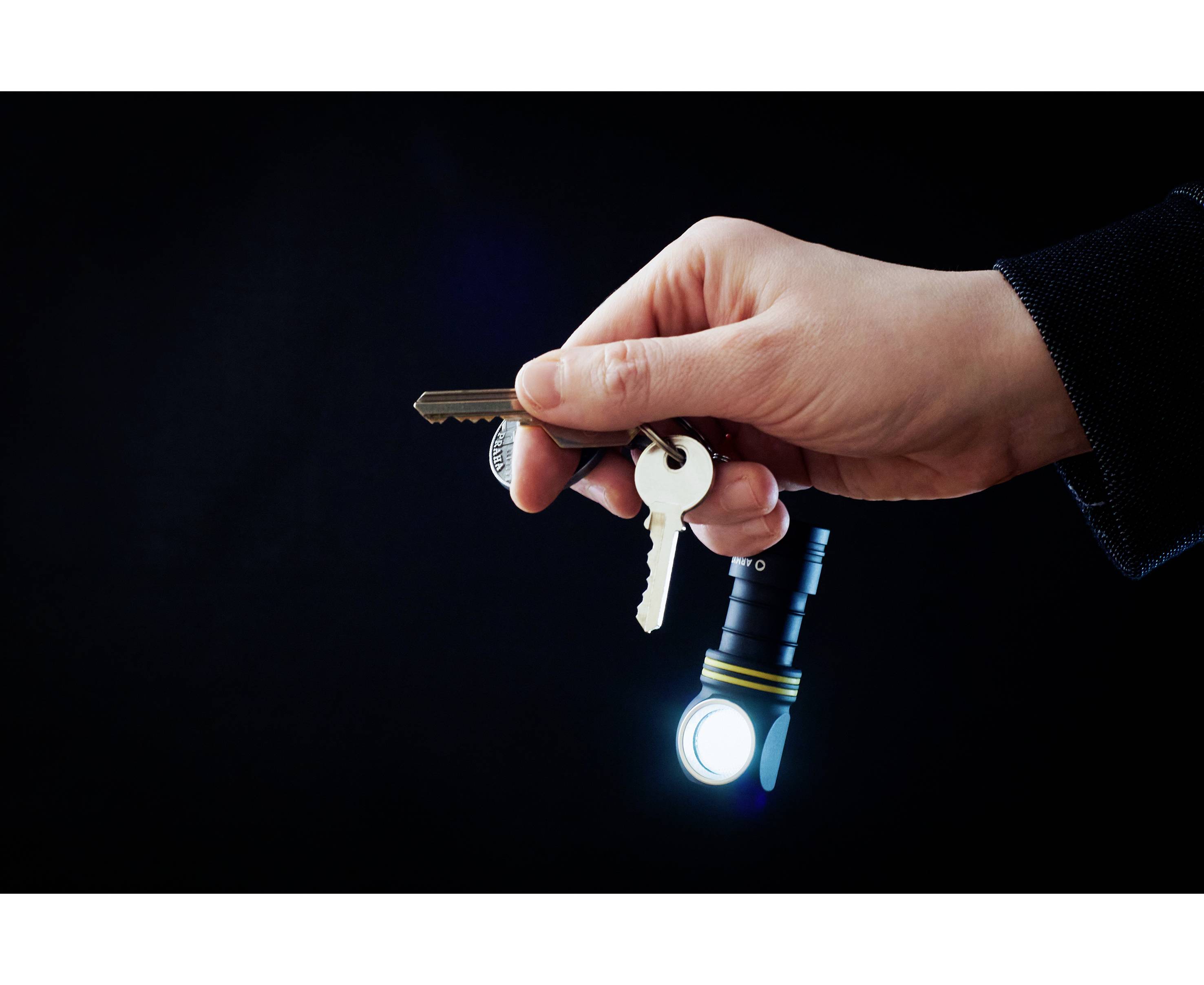 A hand holds two keys and a small torch that is illuminating, against a dark background.