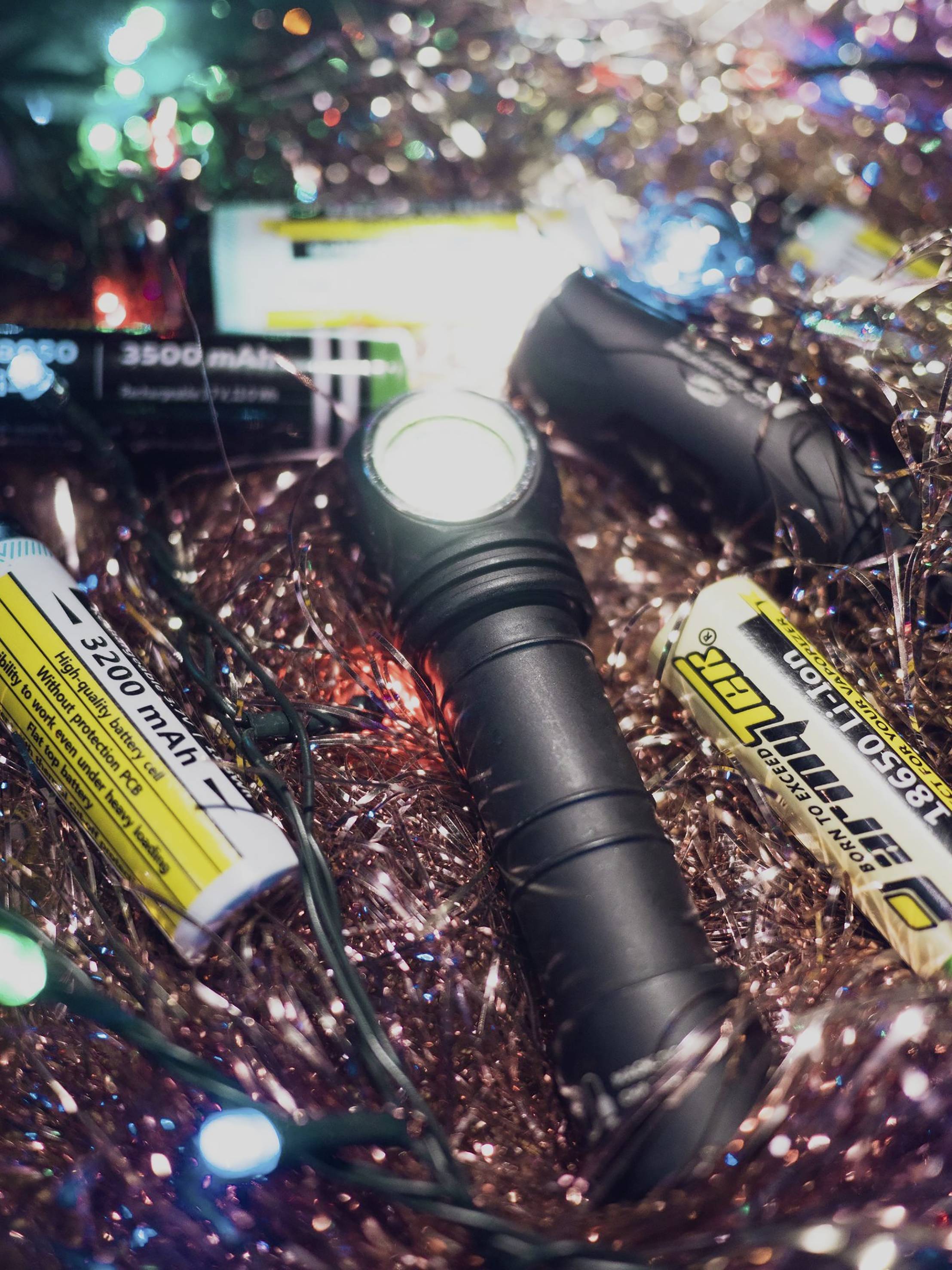 A torch lies amidst shimmering, colourful tinsel and fairy lights, surrounded by batteries.