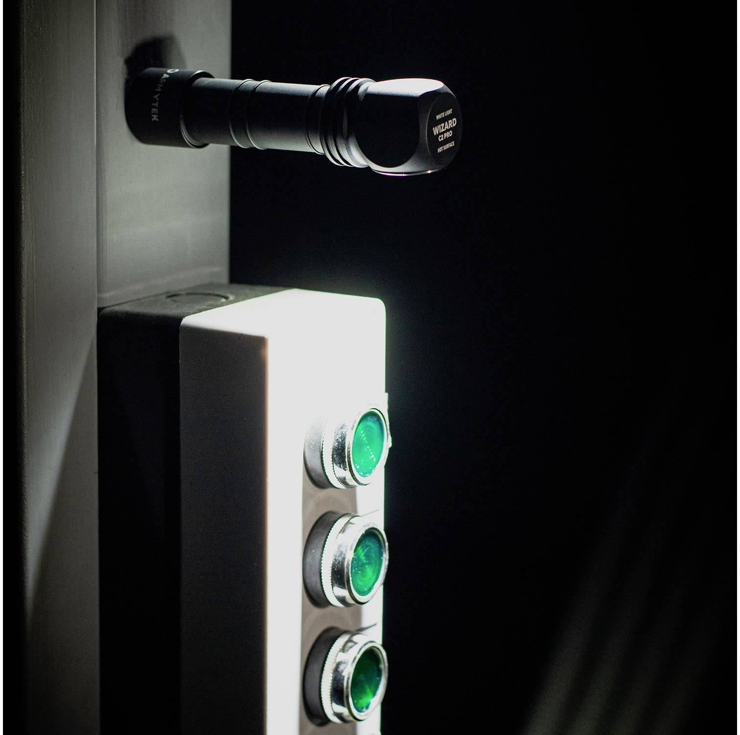 A torch shines on a panel with three green buttons, vertically arranged, in a dark room.