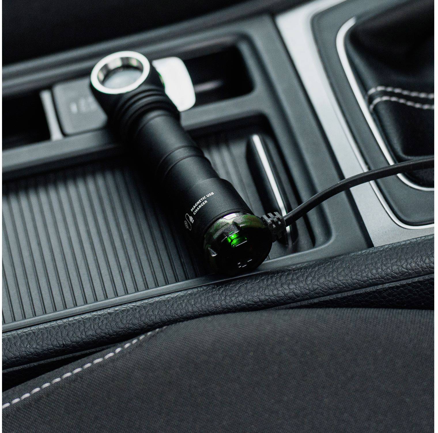 'Torch being charged in the car's cup holder, connected via a USB cable. Interior of a vehicle with black seats.'