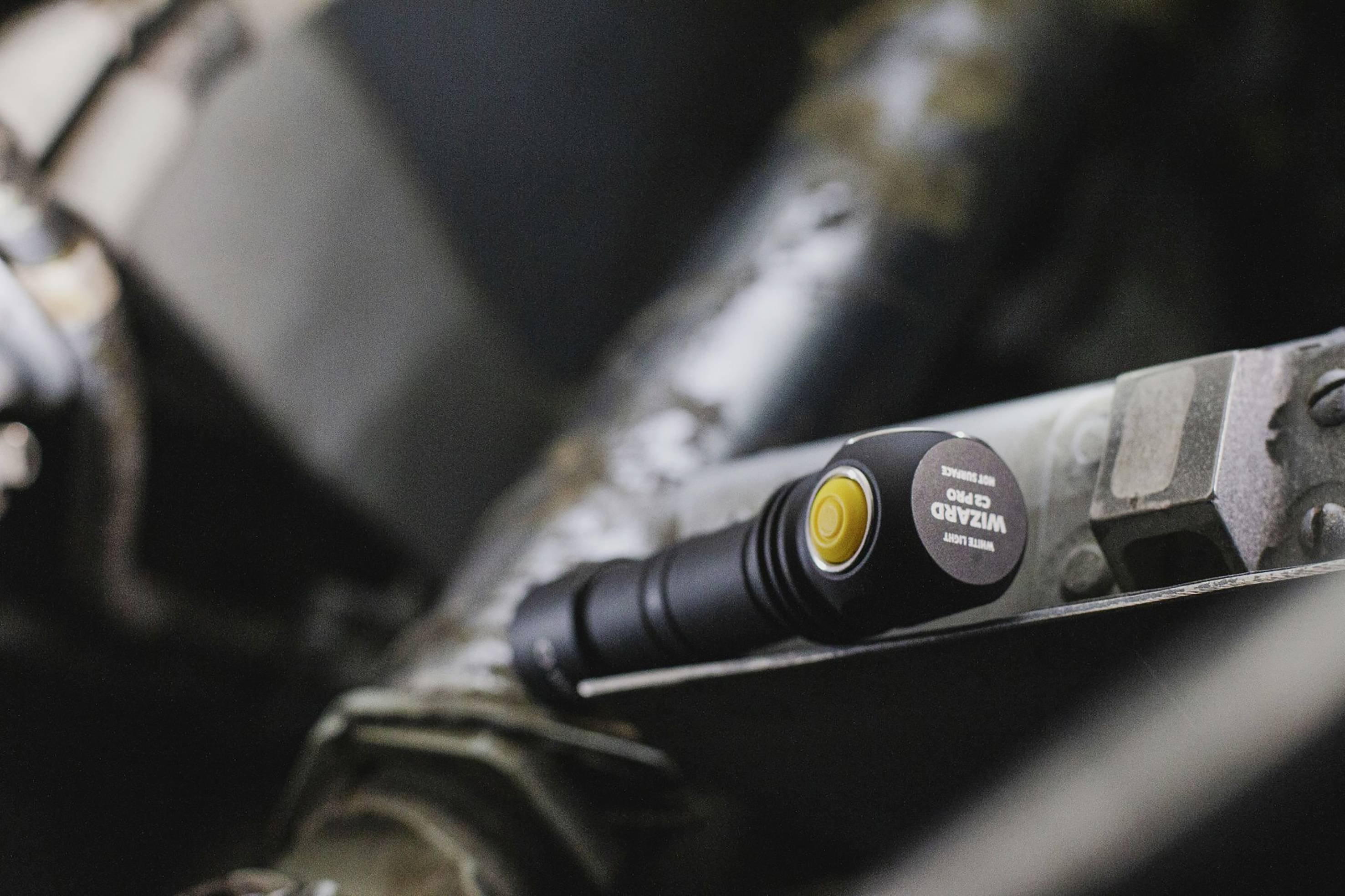 A black torch with a yellow button rests on a metallic surface. It appears to be part of an industrial setting.