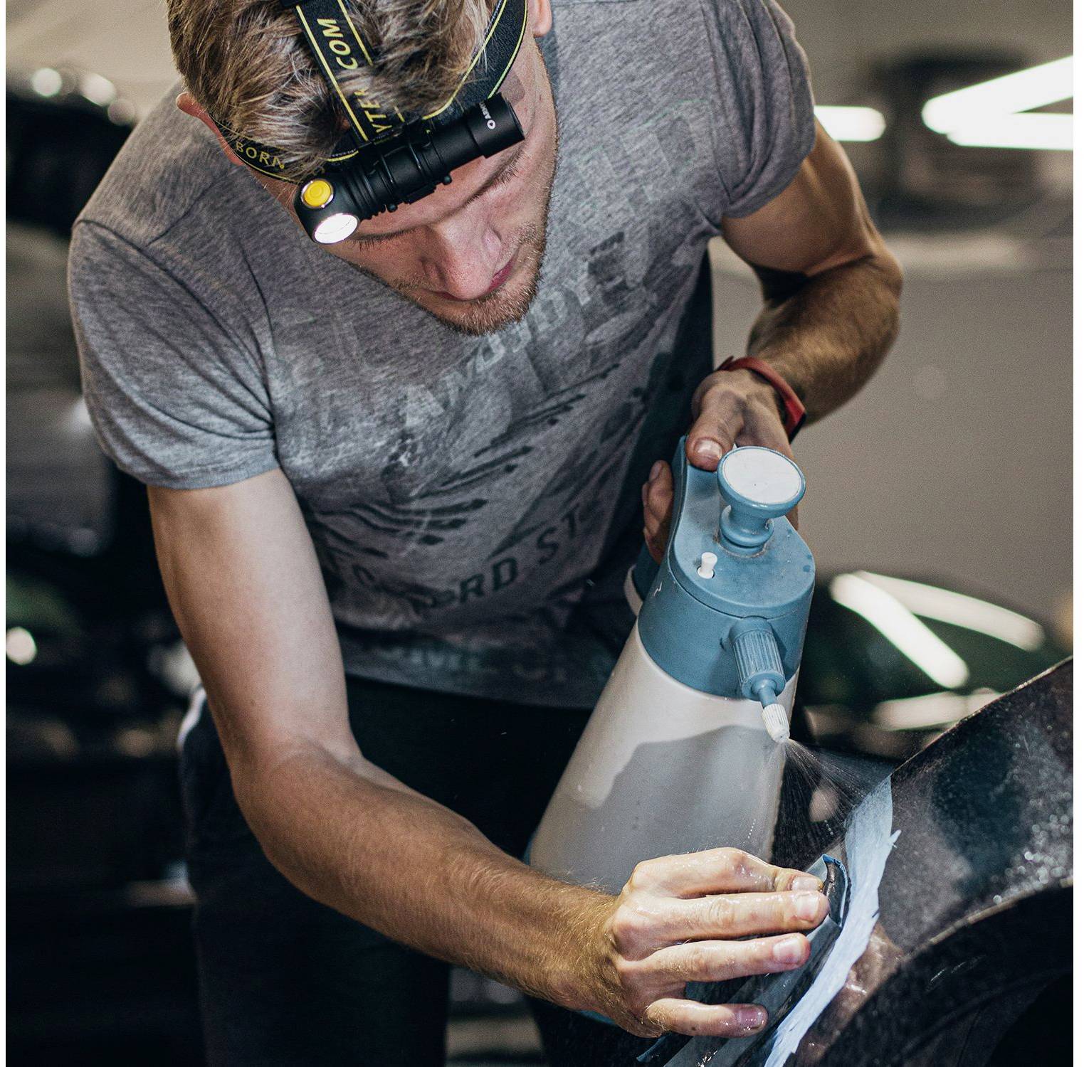 A man is polishing a car with a polishing machine. He is wearing a head torch and working carefully on the bodywork of the vehicle.