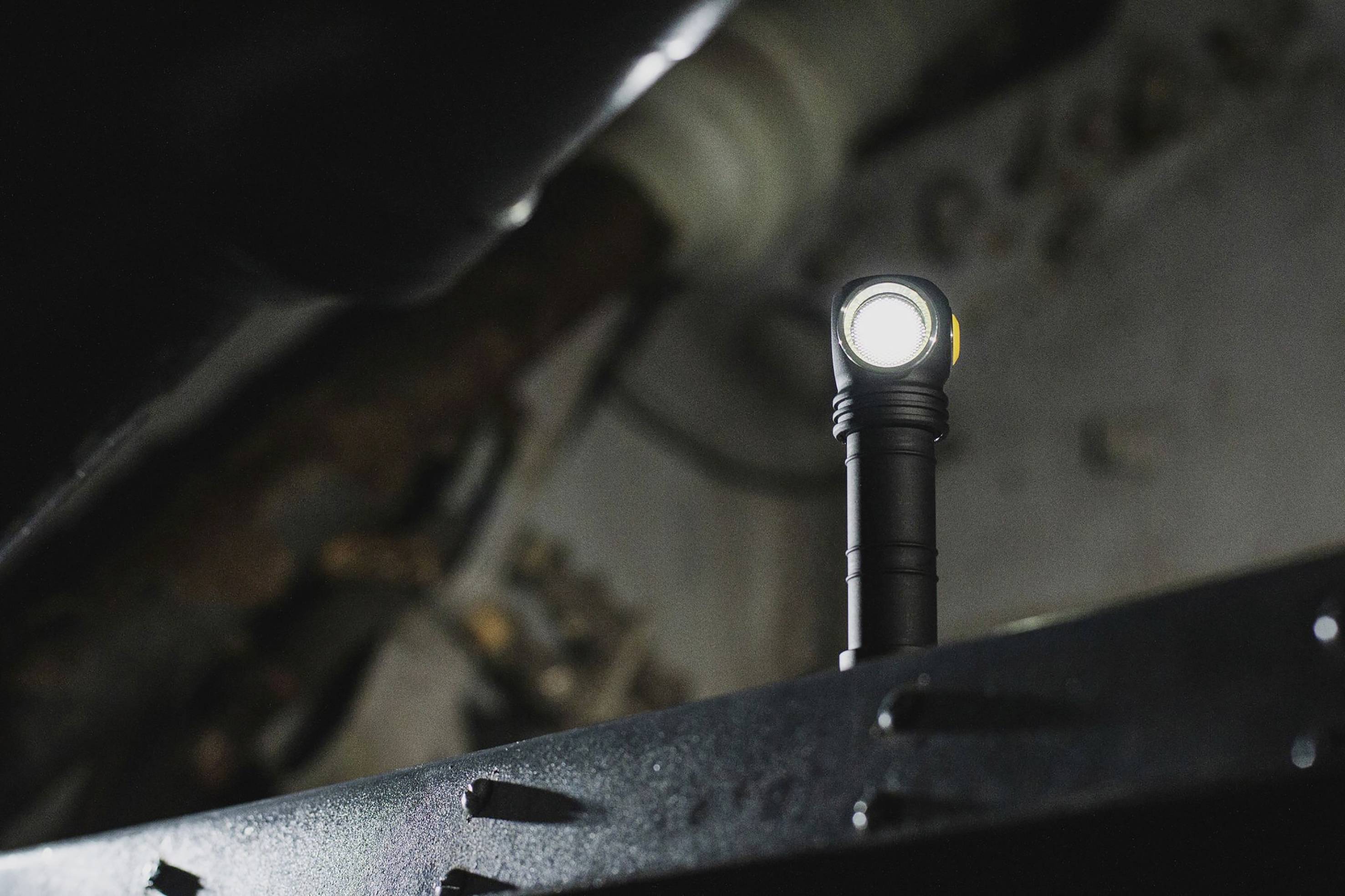 Torch with bright light, standing on a metal surface in a dark room. Background blurred, room details barely discernible.