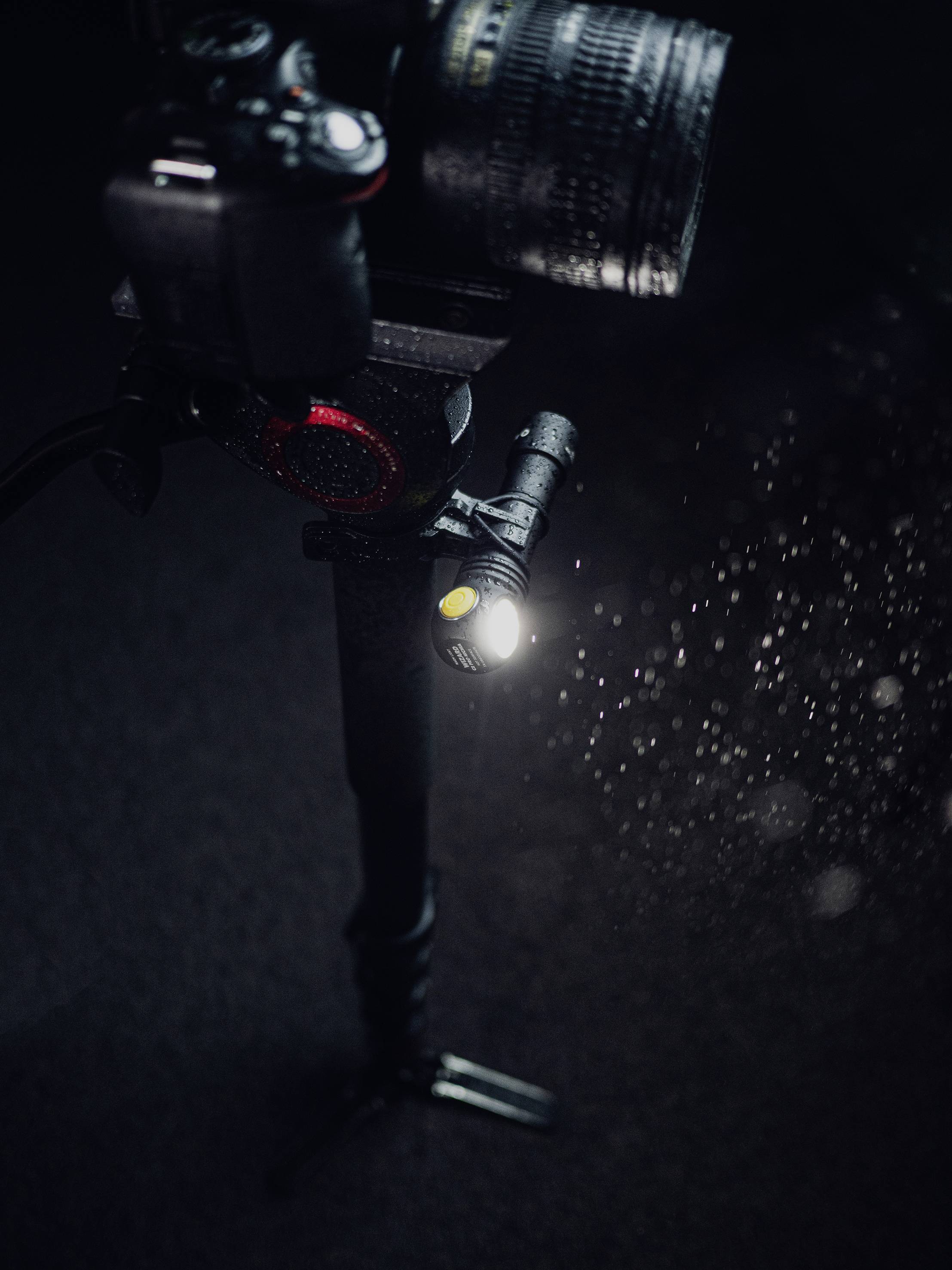 Camera on a tripod with a mounted lens, surrounded by spraying water droplets that glisten in the light.