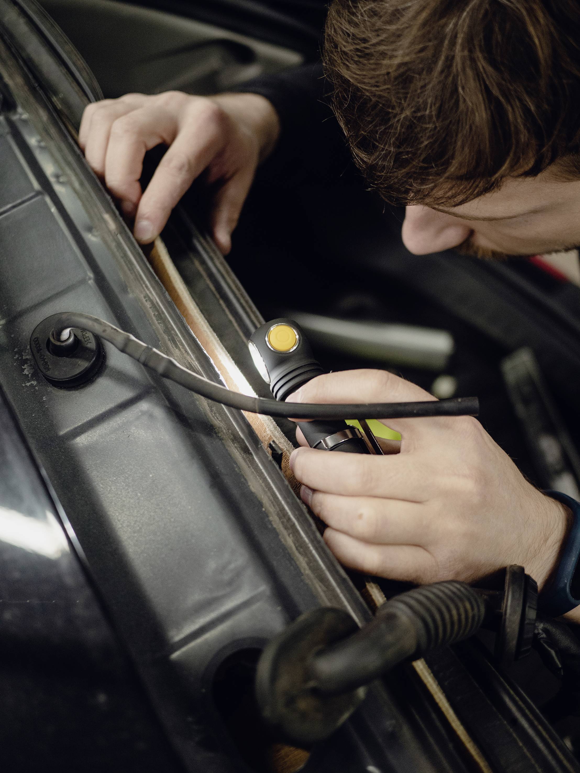 A person is repairing a vehicle, focusing on checking or adjusting wires in the engine compartment.