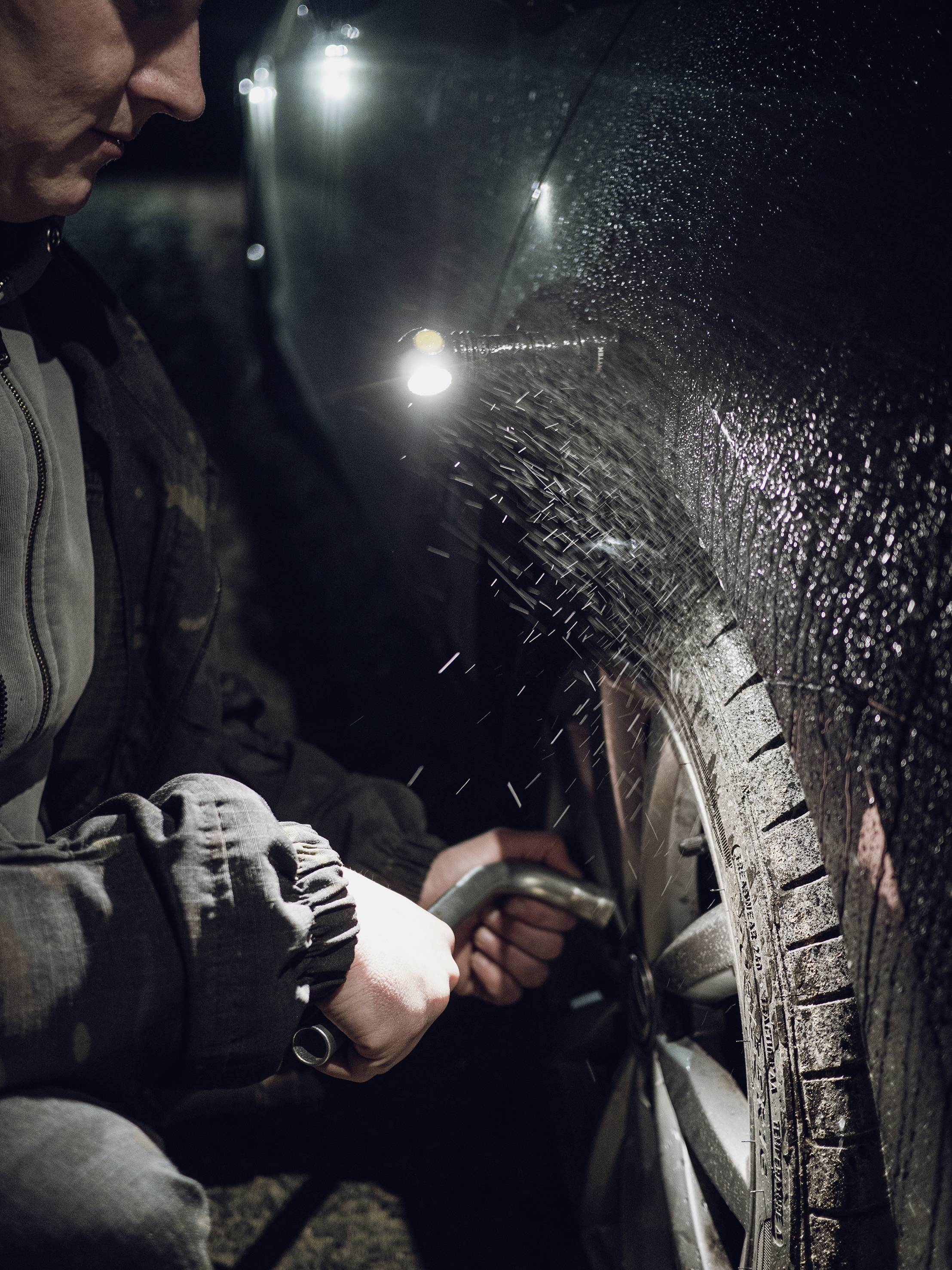 A person is spraying water onto a car's wheel. It is dark, and the light illuminates the water spray and the tyre.