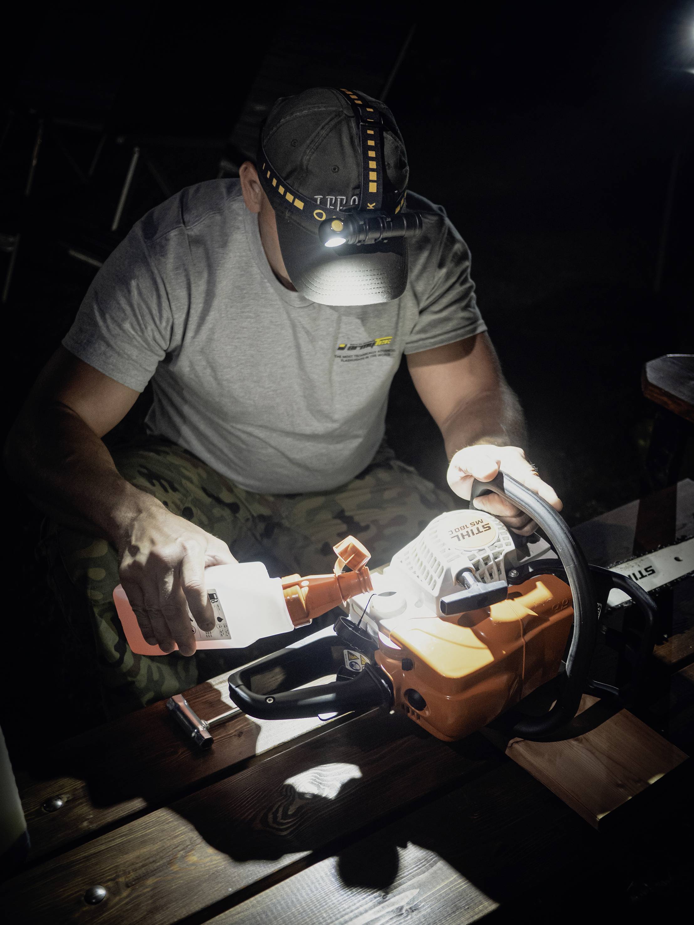 A person is refuelling a chainsaw in the dark using a head torch as a light source.
