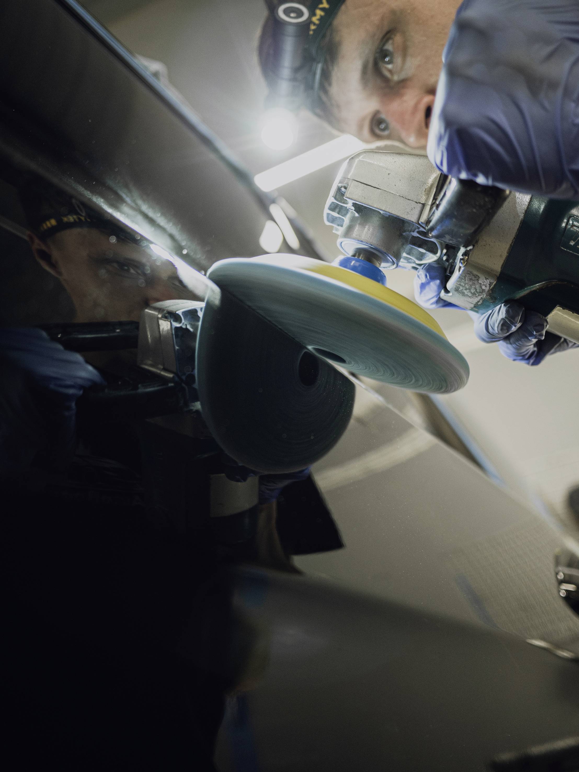 A person is polishing a dark, glossy surface with a polishing machine, focusing on the movement and light reflection.