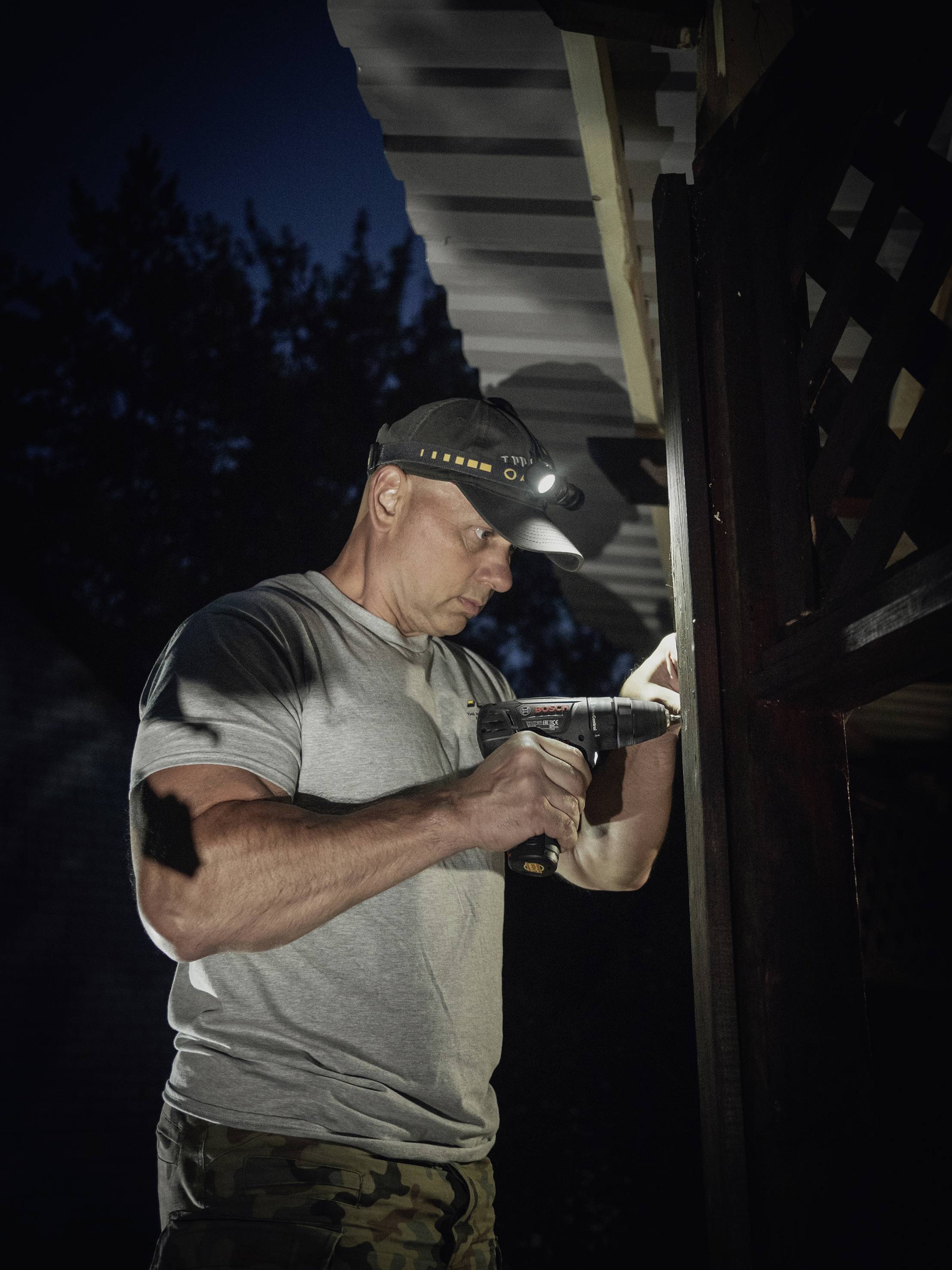 A person is working at night with a drill under a roof. They are wearing a head torch to see better.