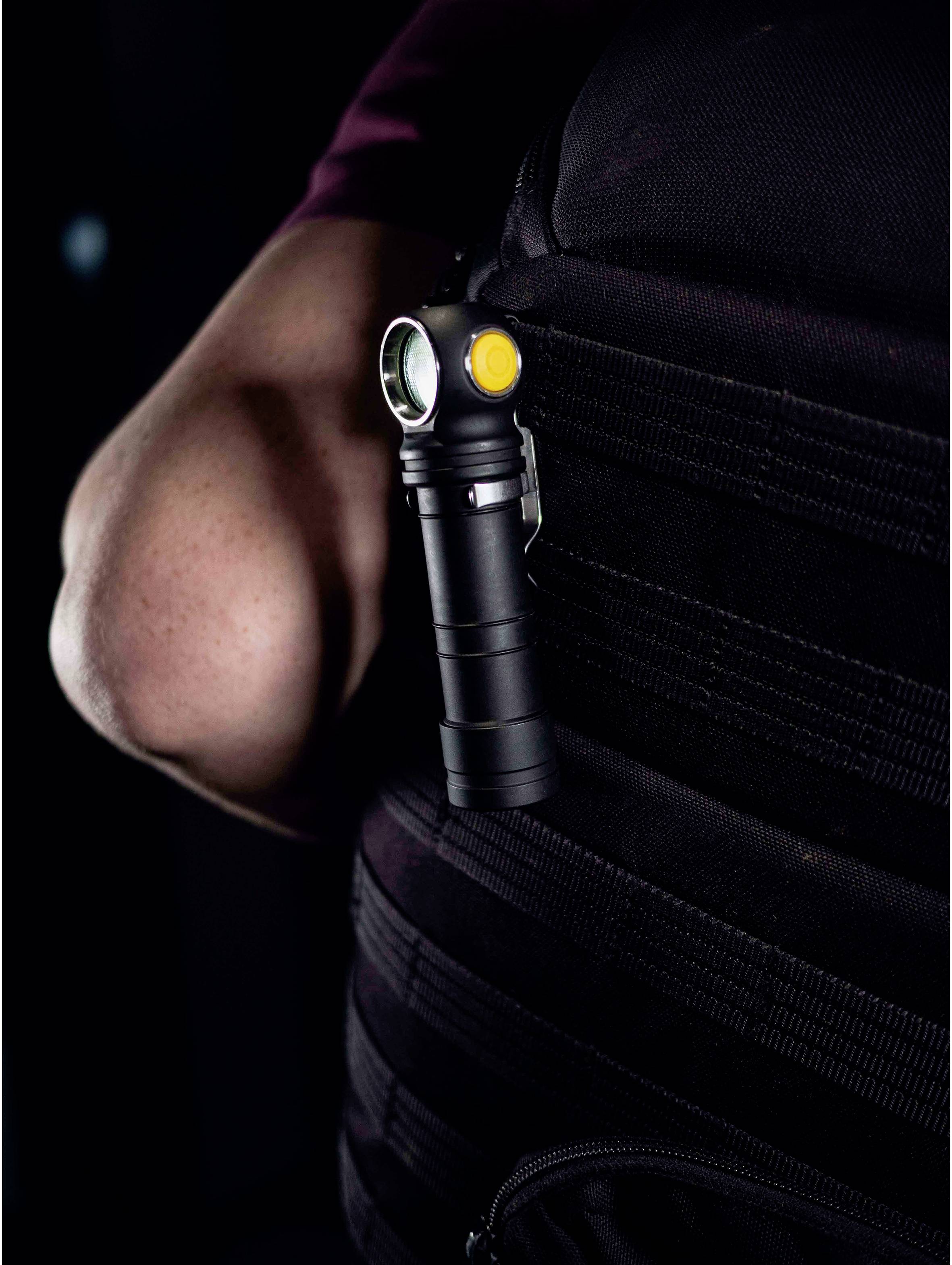 A small, black LED torch with a yellow button is attached to the side of a black rucksack.