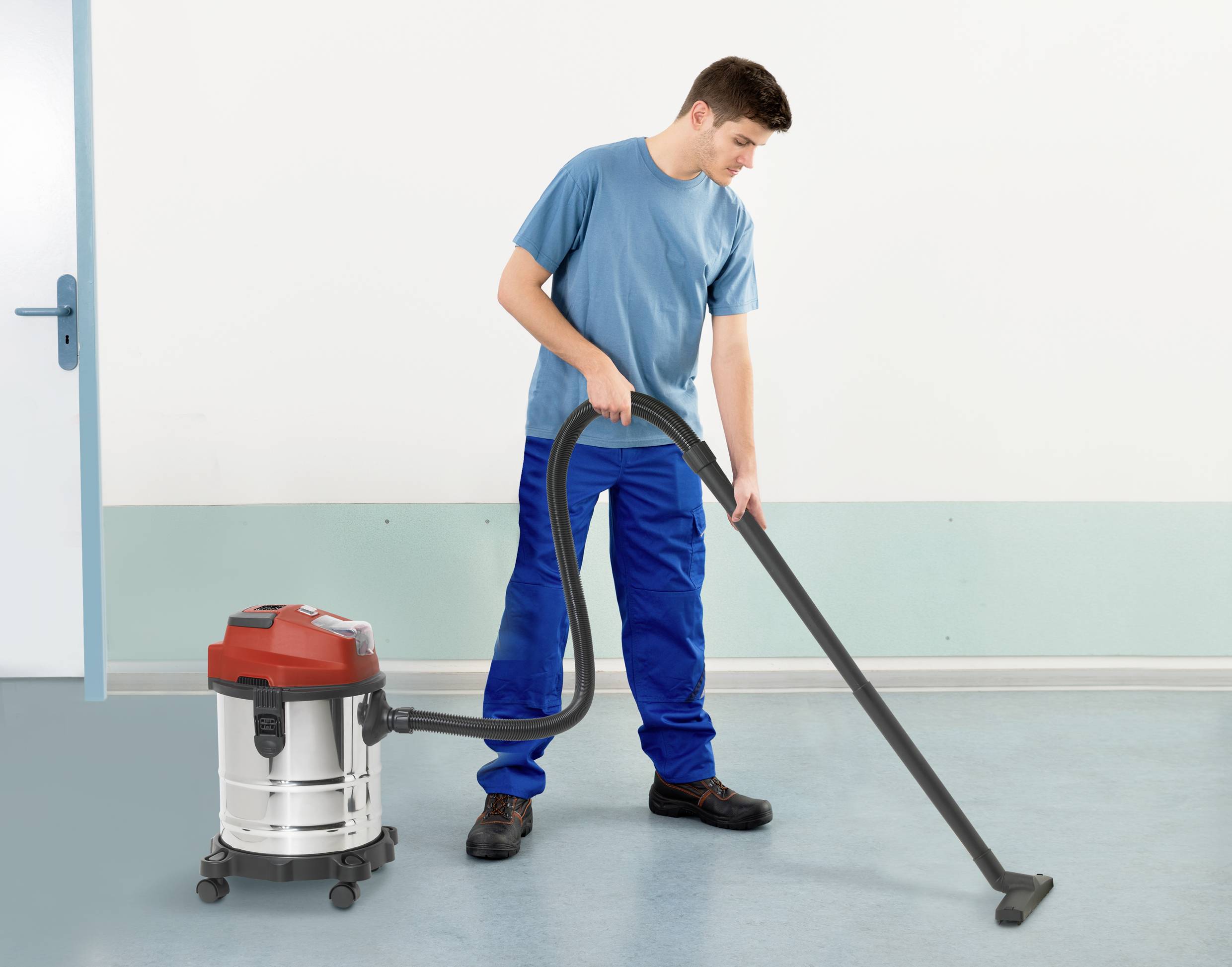 A man is cleaning the floor with an industrial vacuum cleaner in a room with blue walls and a light-coloured floor.