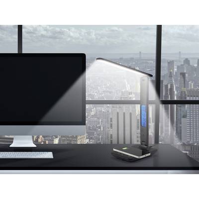Desk with a computer and table lamp illuminating a smartphone. Background: Window overlooking a cityscape.