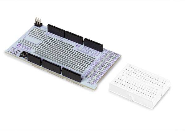 Electronic circuit board with several black connectors next to a white breadboard, suitable for electronic circuits.