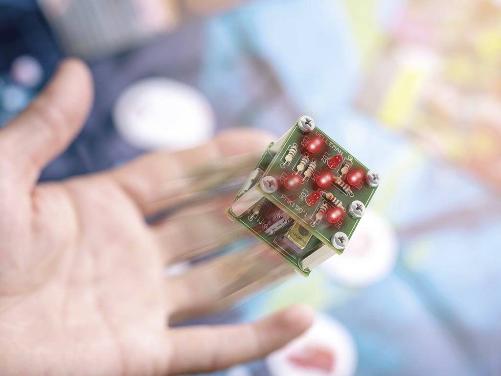 A small electronic circuit with several red LEDs hovers above an open hand. Background blurred.