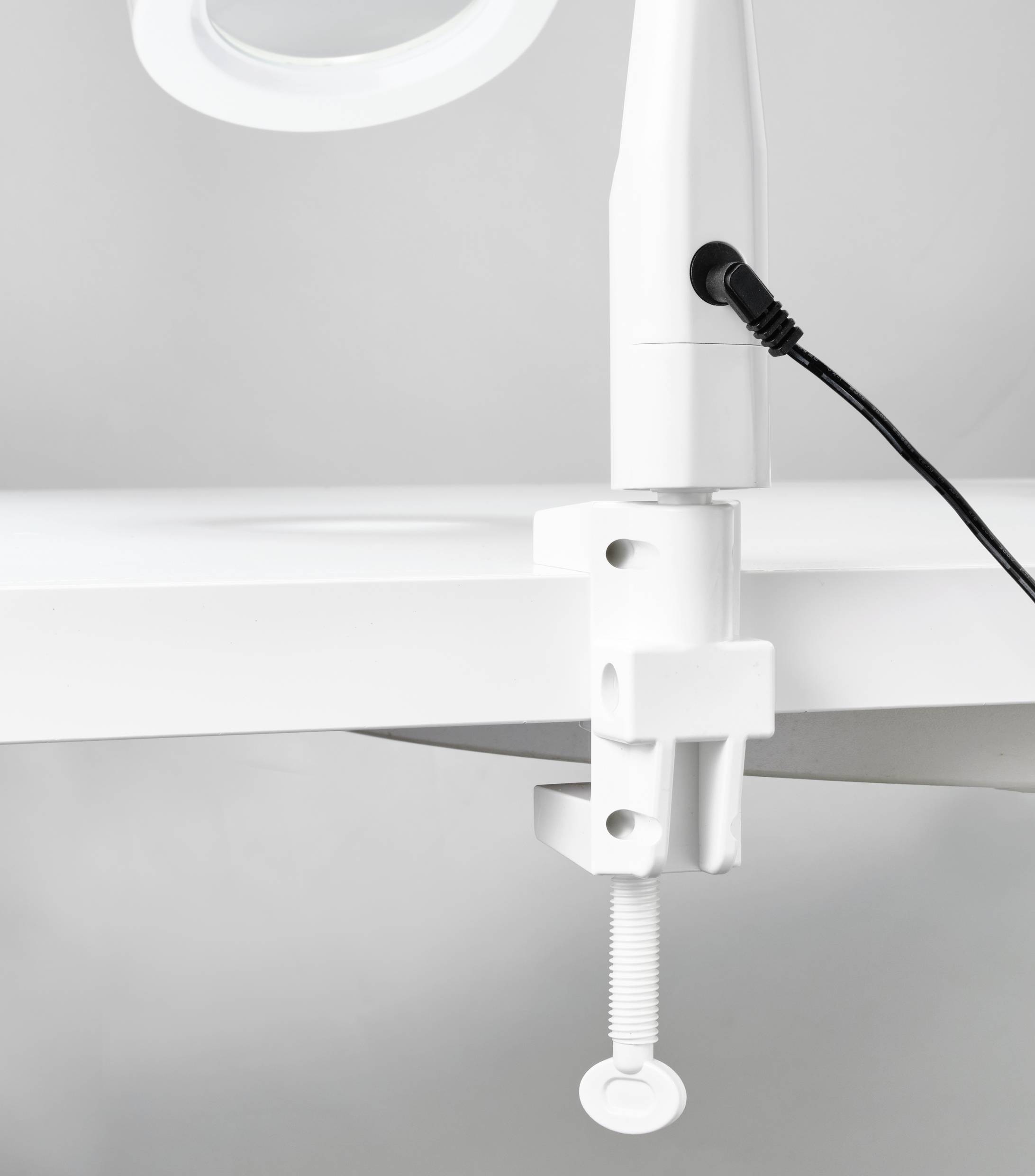 Close-up of a white lamp base with a clamp fitting. The lamp is attached to a table and connected with a cable.