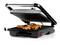An electric tabletop grill with chicken pieces on the grilled surface, lid slightly open.