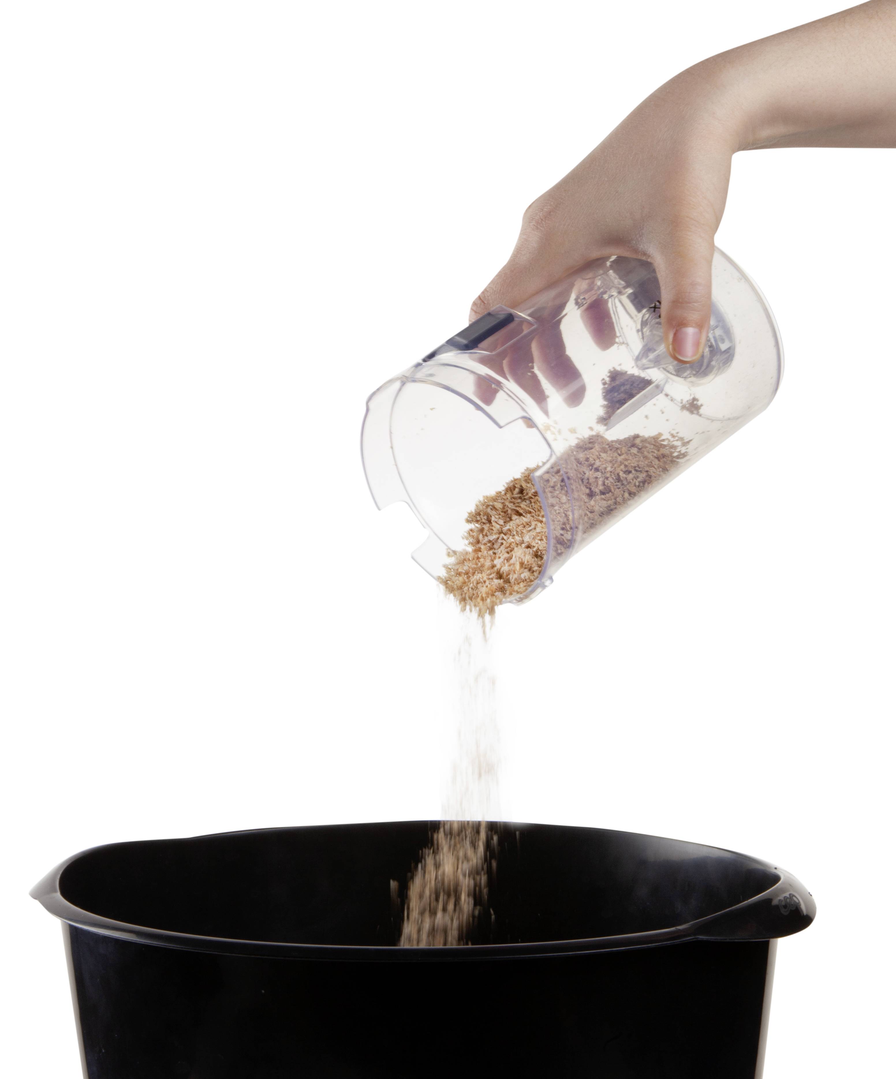 A hand pours oats from a measuring jug into a black bucket.