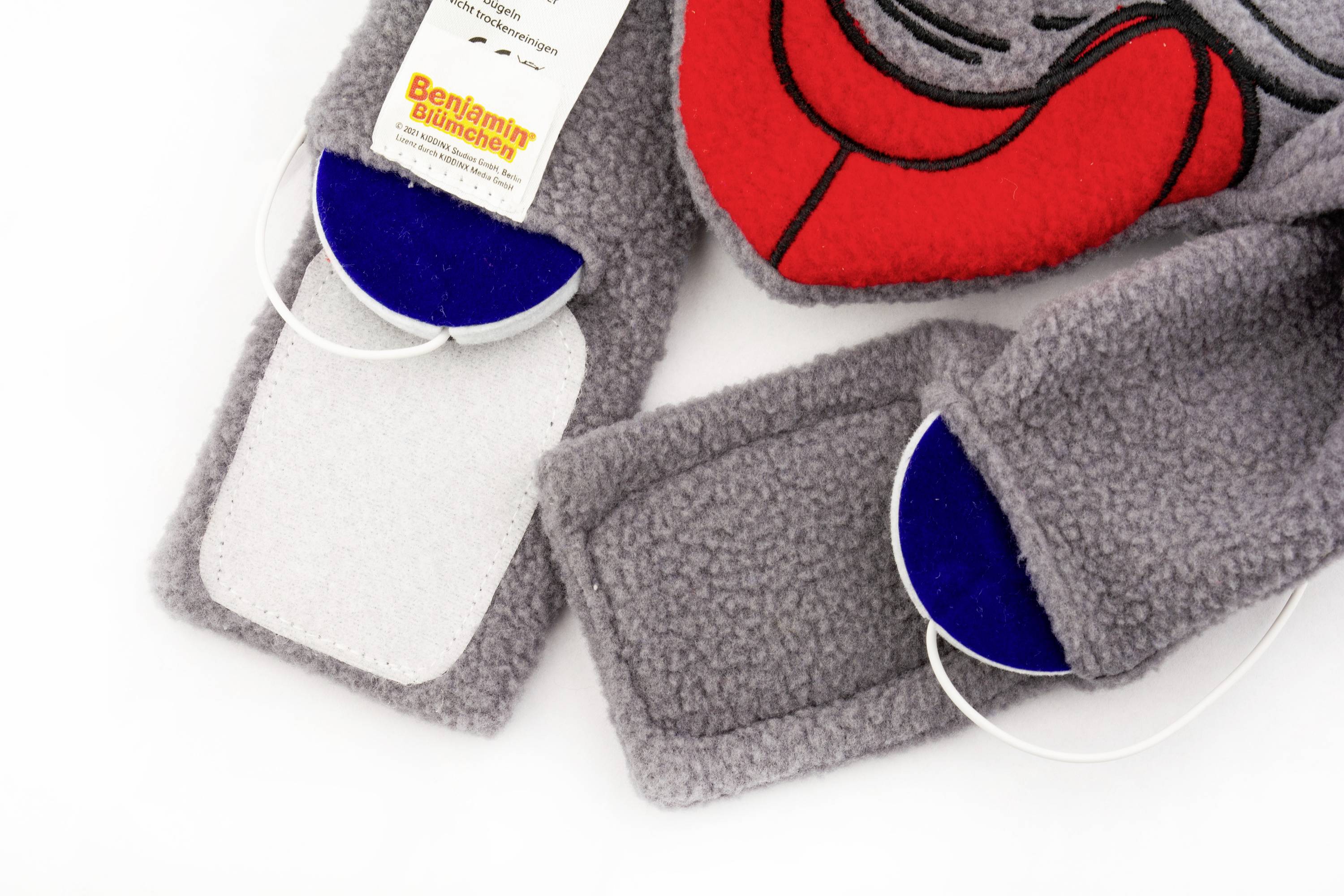 Grey fabric ribbons with hook-and-loop fastenings and blue semi-circles. A label with the inscription 'Benjamin Blümchen Apple Plait' is visible.
