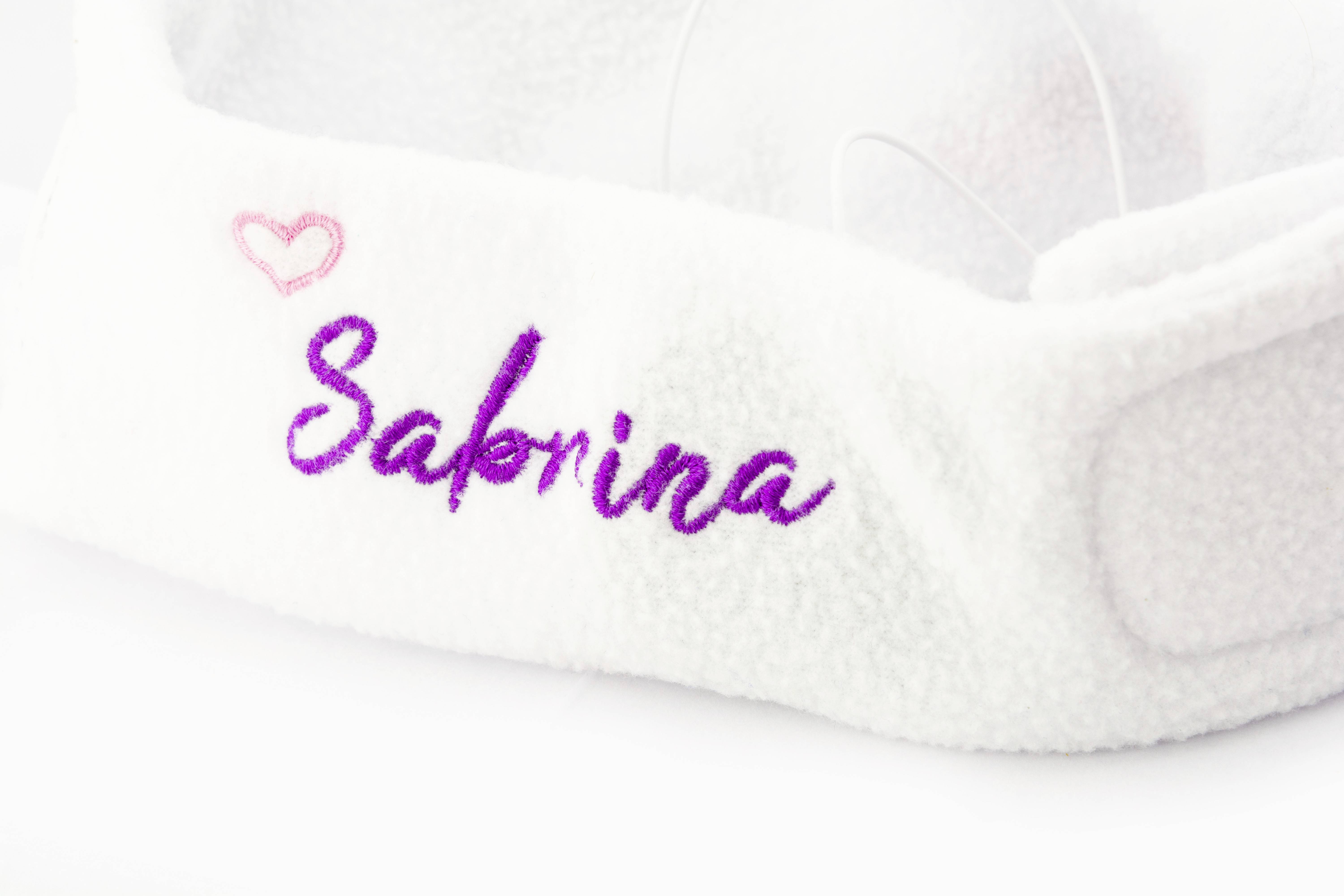 A white plush headband called 'Sabrina' decorated with purple lettering and a small pink heart.