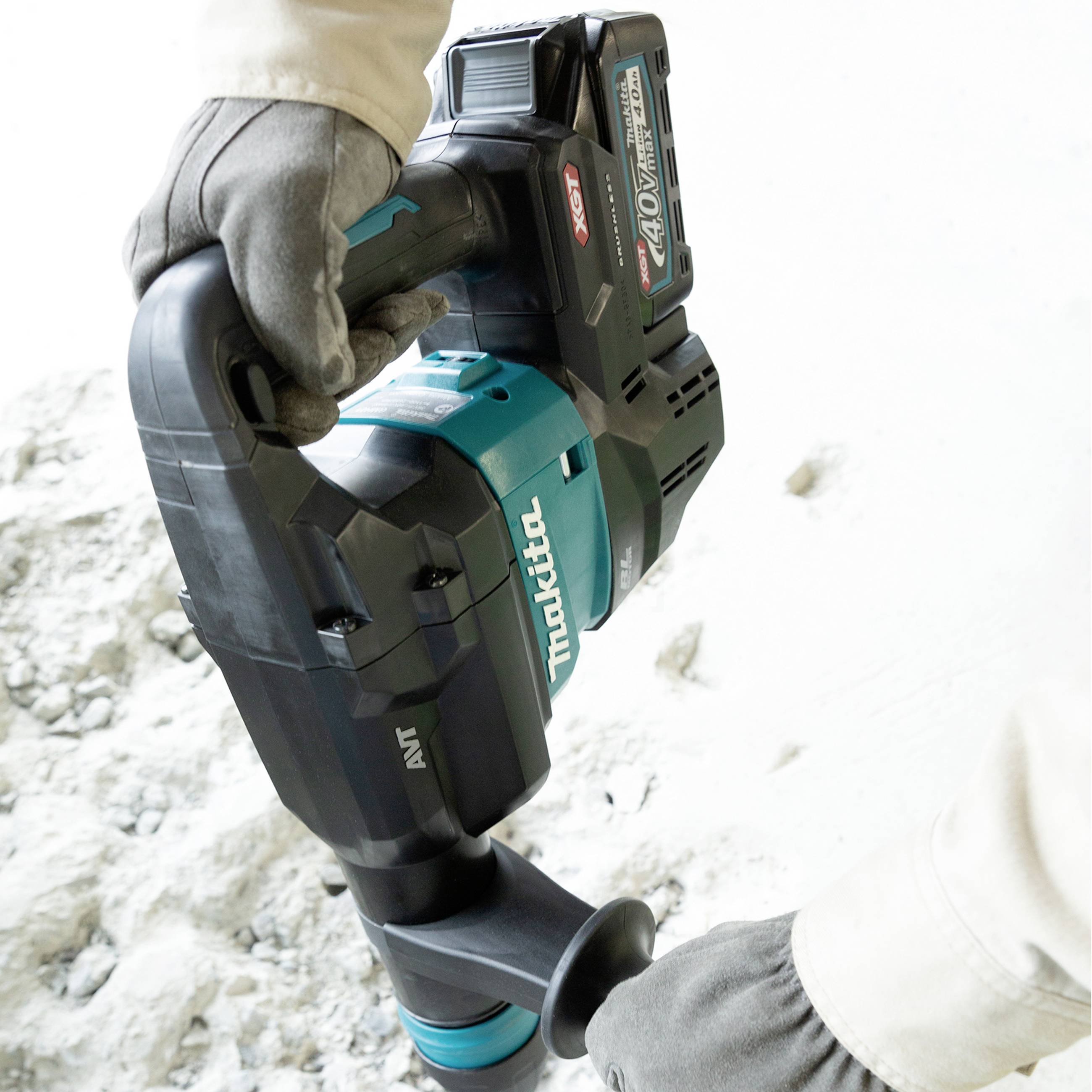 A person is using a Makita electric hammer on a concrete floor, likely during construction or renovation work.