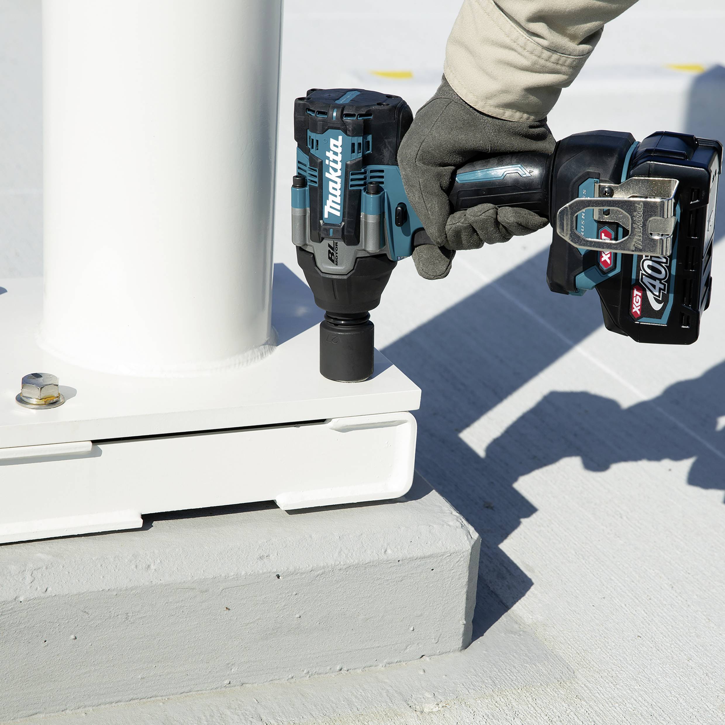A person is using a blue Makita cordless impact driver to secure a screw to a white metal post.