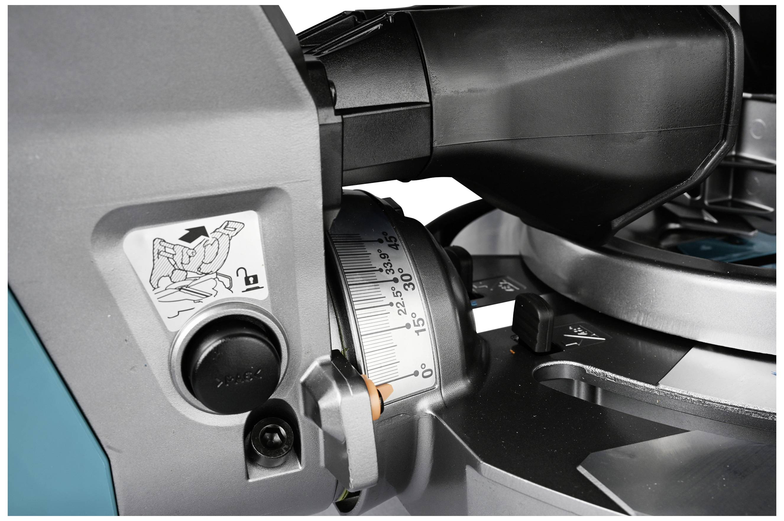 Close-up of a mitre saw with a scale for angle adjustment and locking mechanism. Sticker shows safety instructions.
