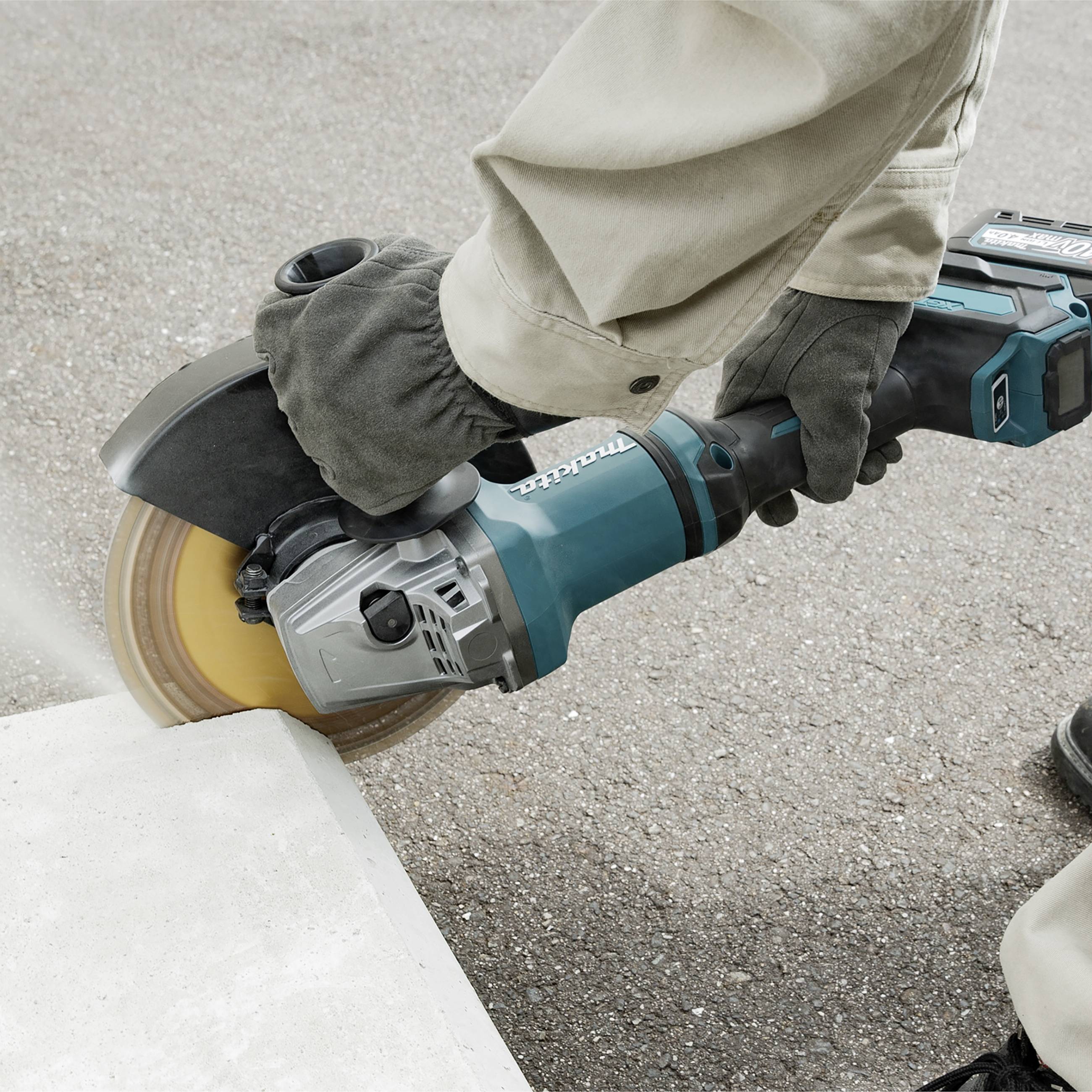 An angle grinder is being used by a person on concrete. The device is in motion and generating dust.