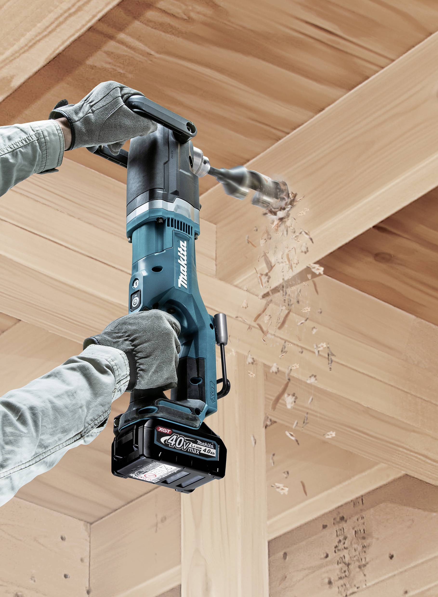 A person is drilling a hole in a wooden structure using a cordless drill. Wood shavings fly as the tool operates.