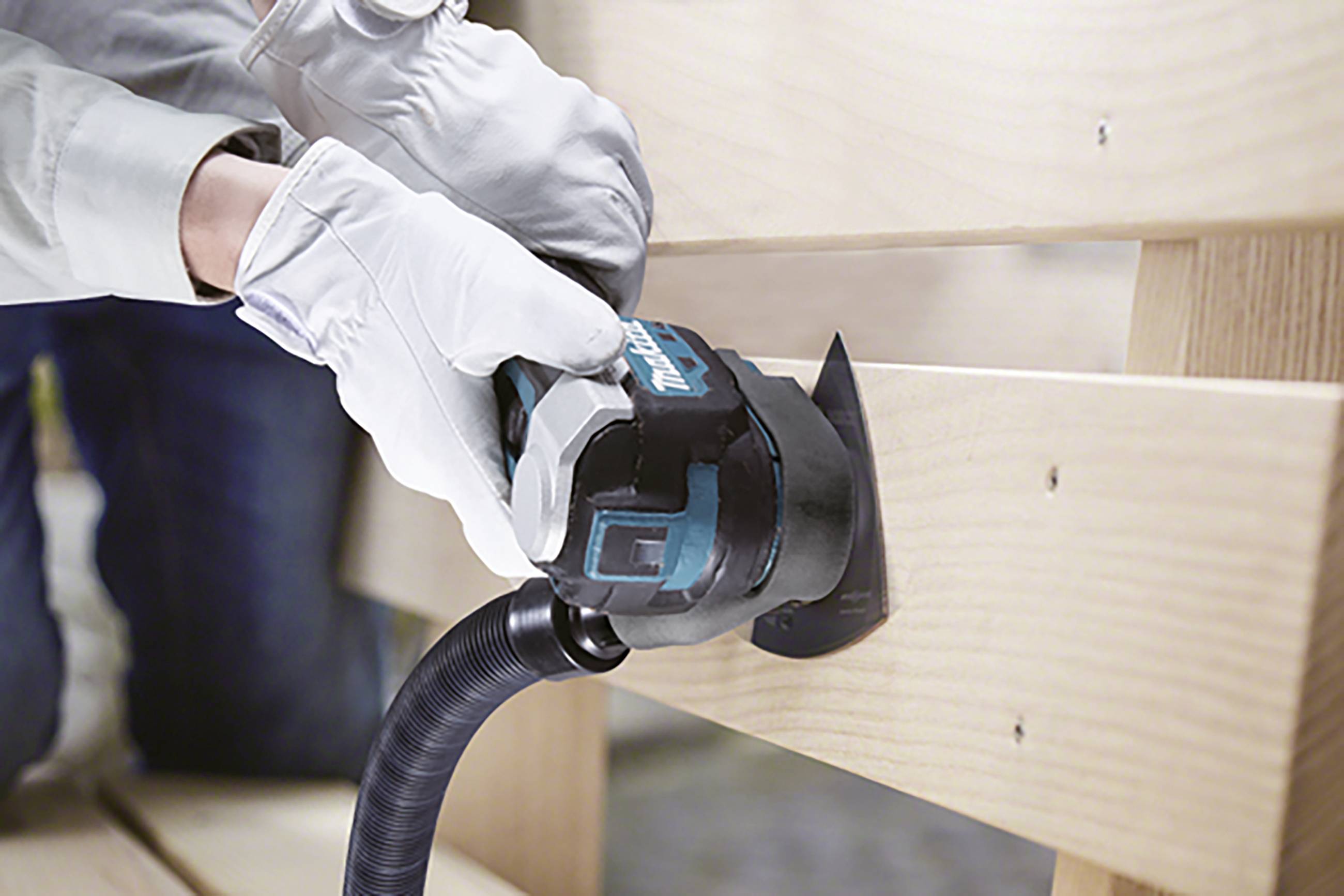 A person is sanding a wooden surface with a blue electric sander. They are wearing white gloves.