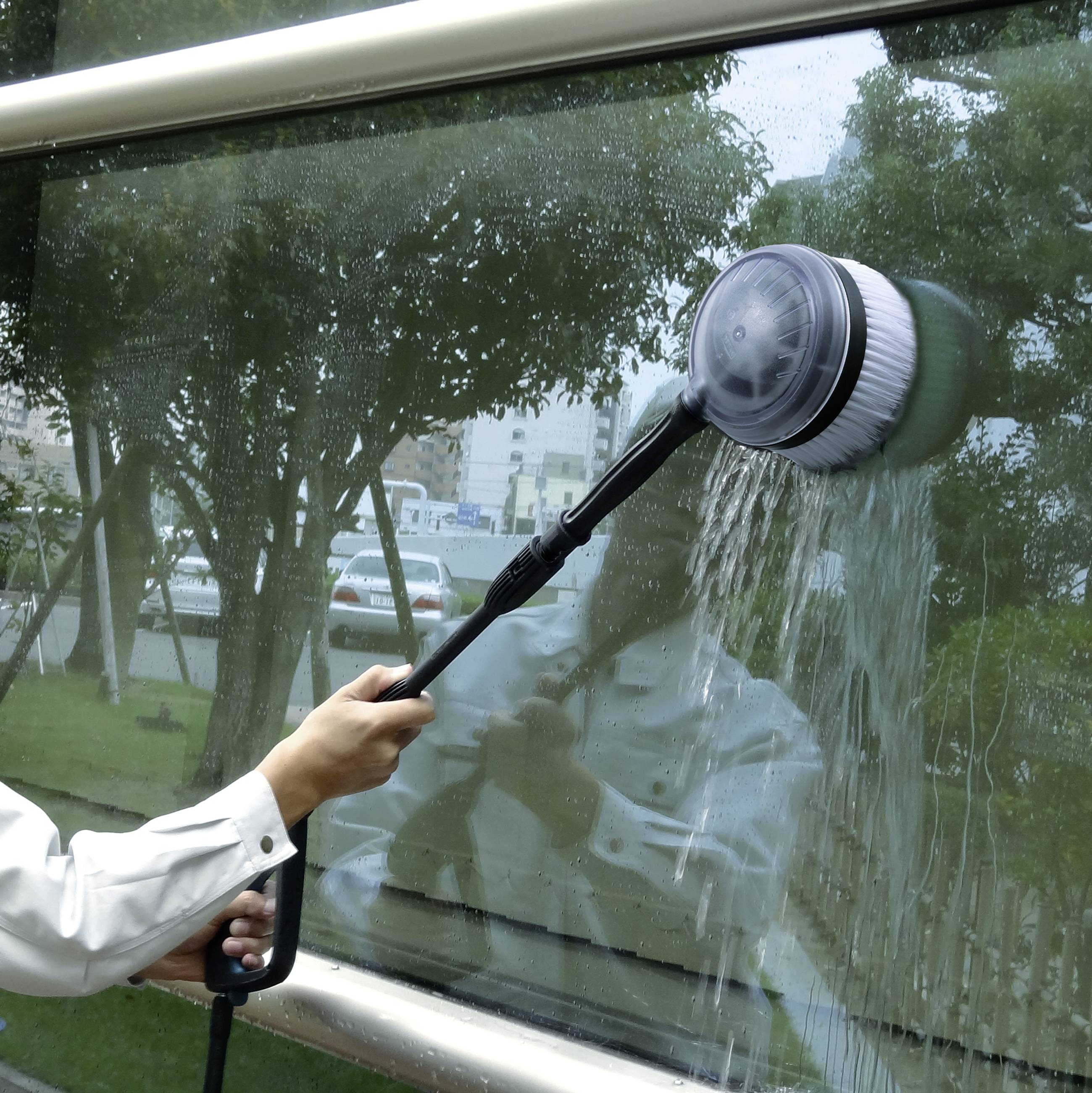 A person cleans windows with an electric brush; the background shows a blurred urban landscape.