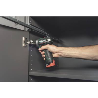 A person is using a cordless drill to secure a hinge on a grey cabinet.