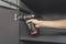 A person is using a cordless drill to secure a hinge on a grey cabinet.