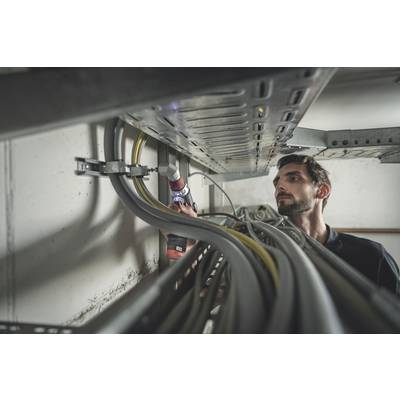 A man is working on a cable trunking system in a technical room, using an electric tool. Cables run along the wall.