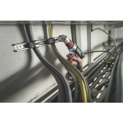A hand holds a drill and tightens cables within a metal frame. Various cables run parallel along the wall.