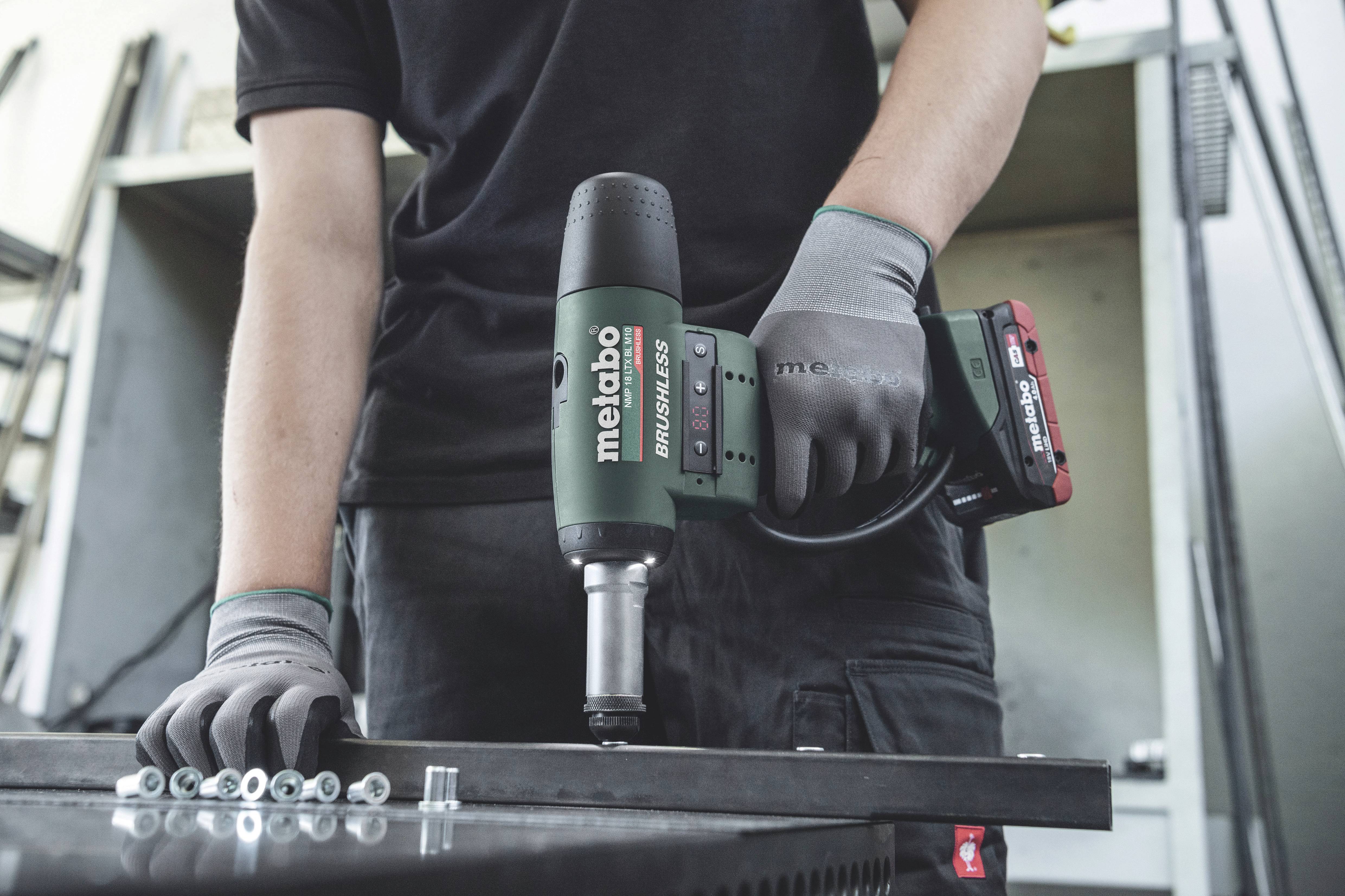 A person is holding a green Metabo power tool with '11.0 Ah' written on it and is working on a metal piece, with a workshop visible in the background.