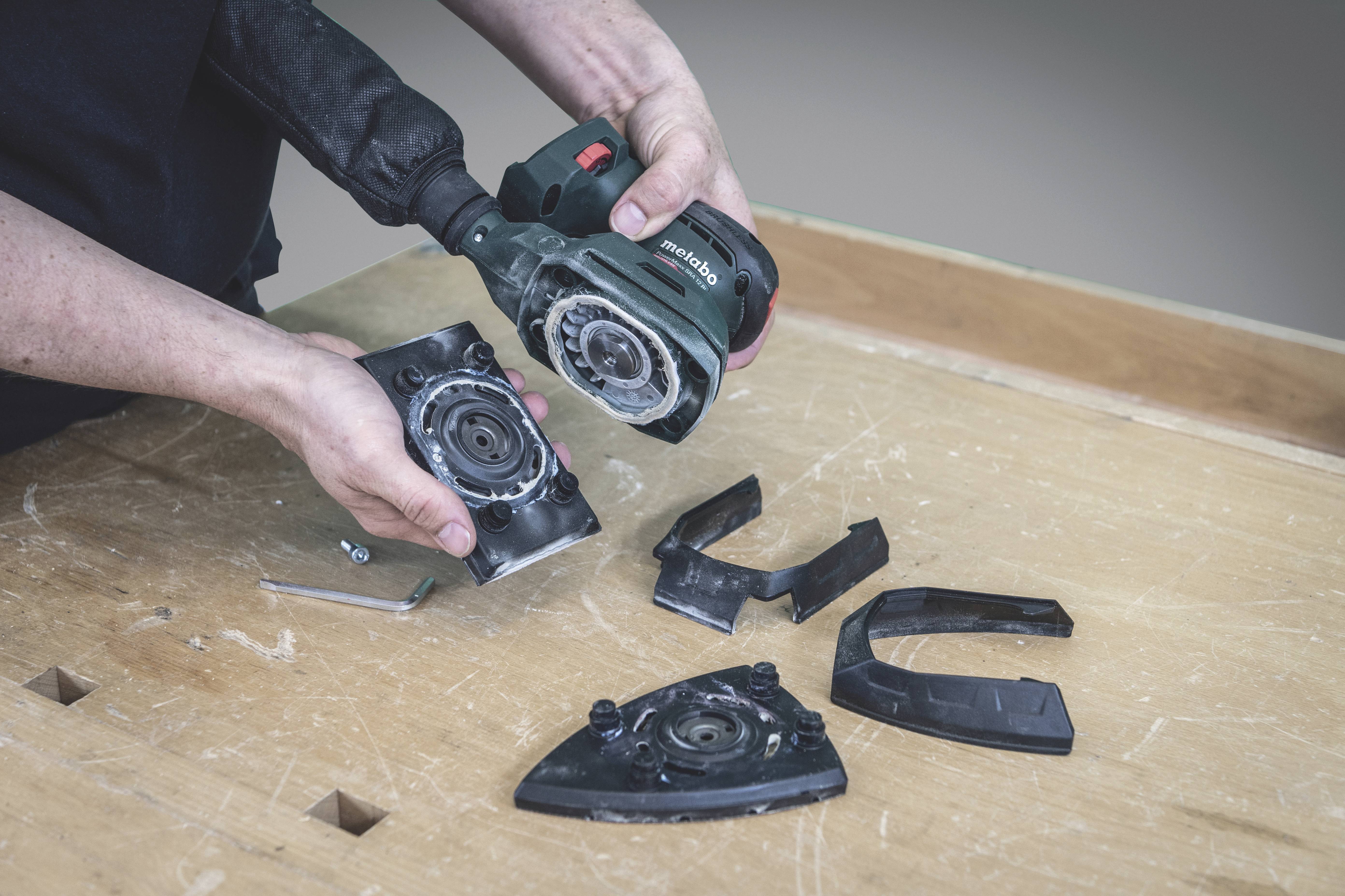A person is holding an angle grinder with the guard removed. Various parts are lying on the table.