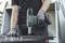 A person is holding a Metabo cordless drill and working on a metal table. Screws are lying on the work surface.