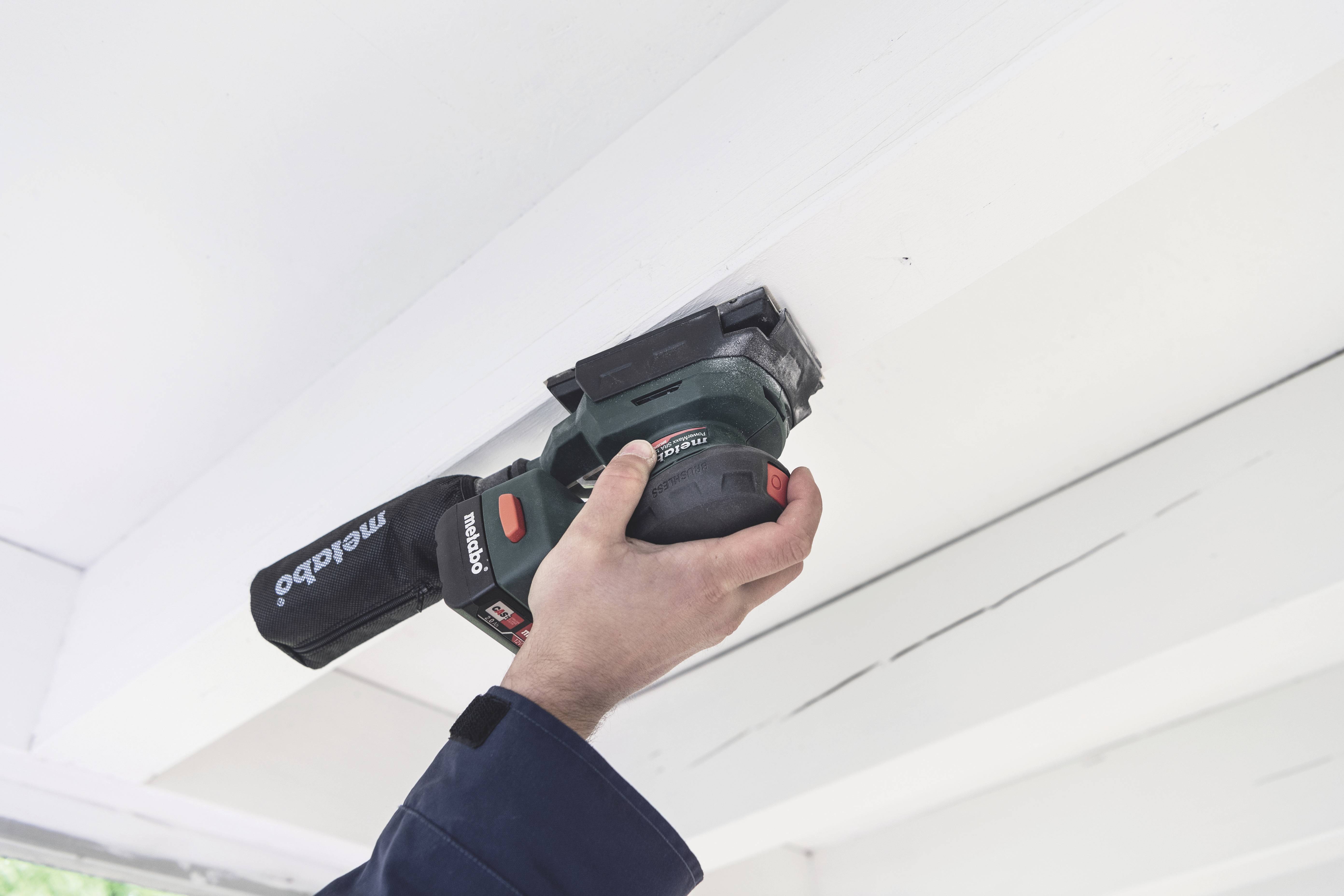 A person is grinding the surface of a beam with an electric tool. The beam has visible cracks.